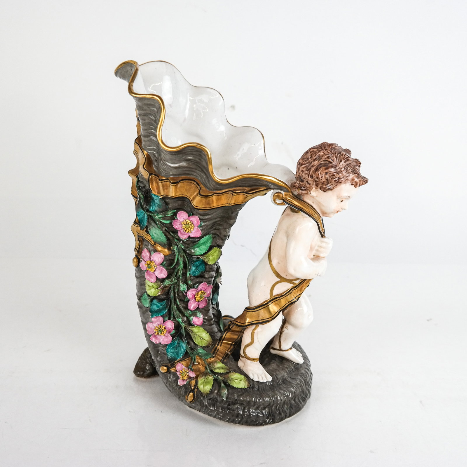 Paris Porcelain Figural Vase: Paris porcelain figural vase of putto pulling a flower decorated cornucopia [10.5" x 7.5" W x 5" D] Overall condition is good, wear commensurate with age, minor losses to flowers.