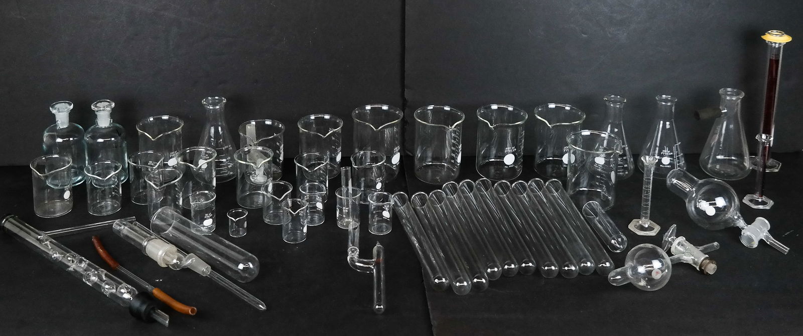 Pyrex & Other Assorted Chemistry Wares, 56: Pyrex and other assorted glass chemistry wares comprising 23 beakers in various sizes, four flasks, two stoppered decanters, 12 test tubes, three graduated cylinders, three stoppers, and nine other tu