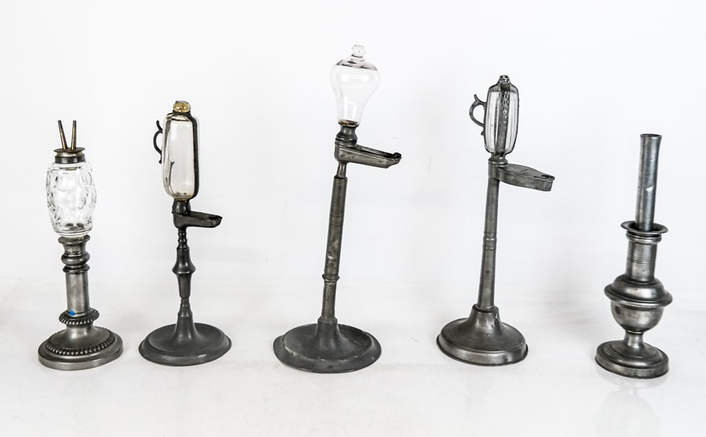 Pewter Whale Oil Timekeeping and Other Lamps, 5: Five pewter whale oil lamps, 19th century, comprising two timekeeping lamps with pewter frames and stands, with impressed roman numerals to bands around bulb, an oil lamp with a cut glass bulb, an oil