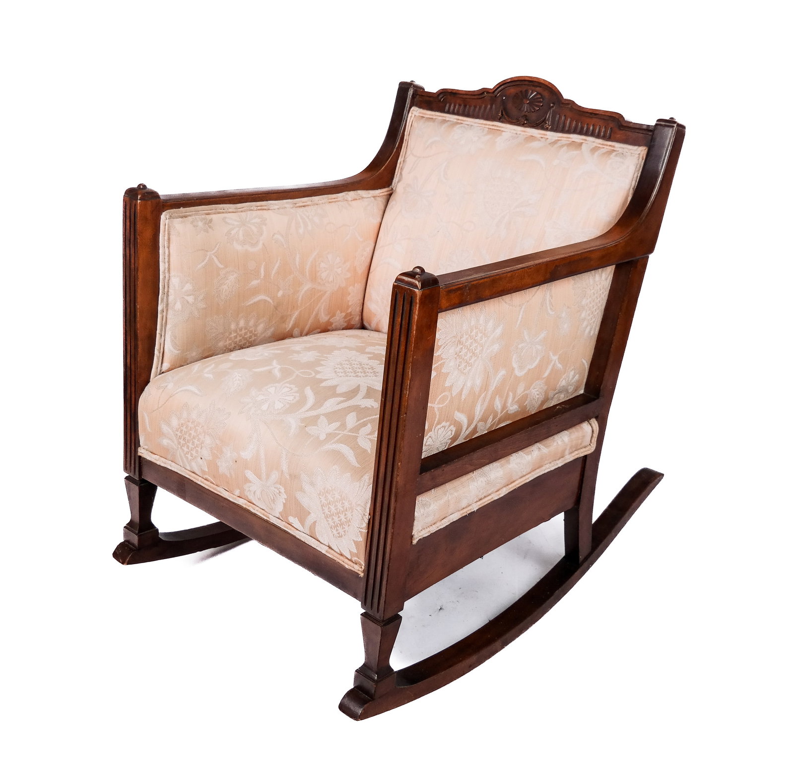 Carved Mahogany and Upholstered Rocking Chair: Carved mahogany and upholstered rocking chair, early 20th century, with a carved crest, fluted arm supports, and floral upholstery. [33.5" H x 24.75" W x 36" D; seat height: 21" H]. Condition is good 