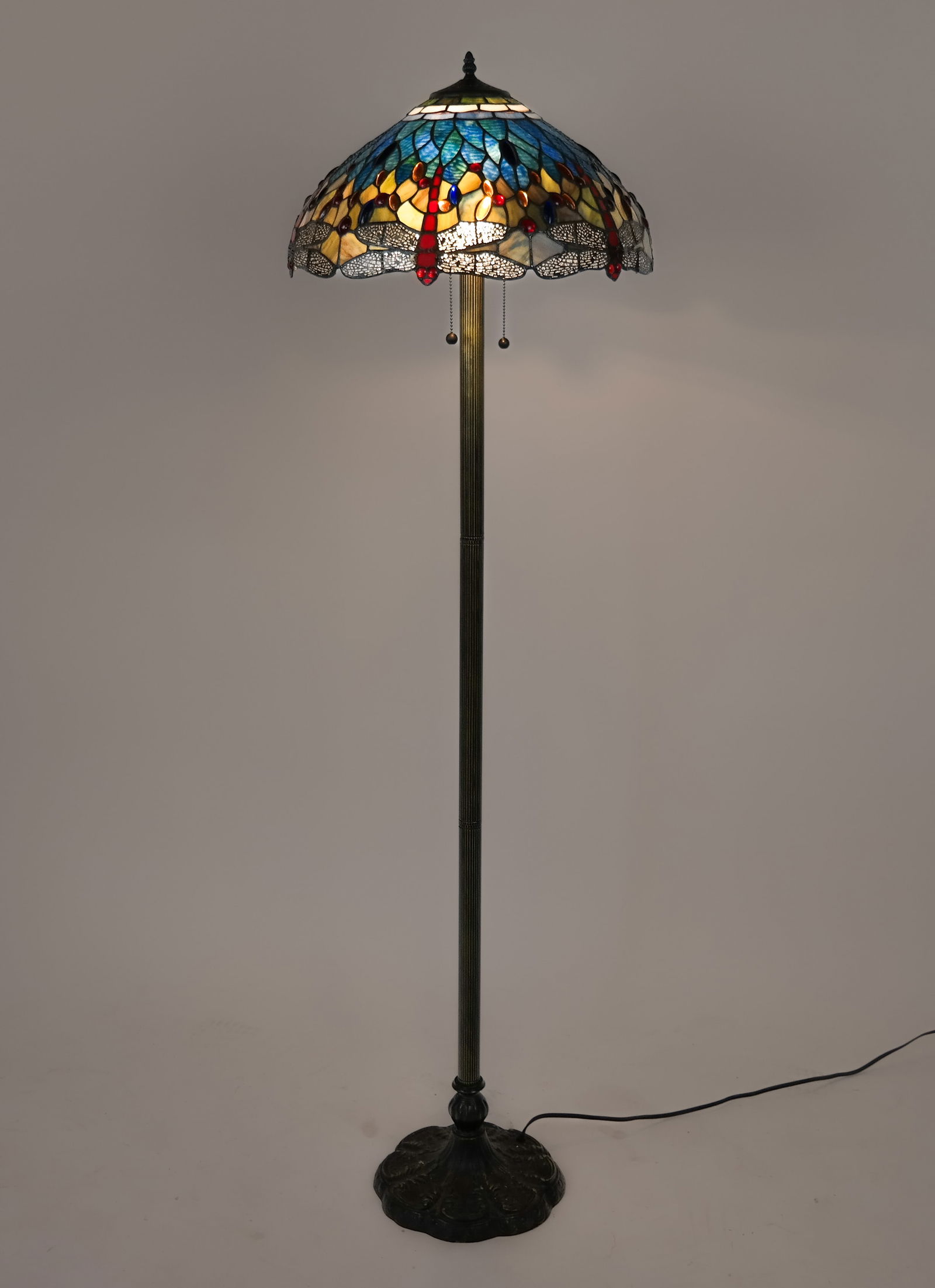 Stained Glass Floor Lamp with Dragonflies: Stained glass two-light floor lamp, 20th century, with dragonfly and glass cabachon decoration and a patinated metal base and stand. [63" H x 17.5" Diameter]. Condition is good with some warp to shade