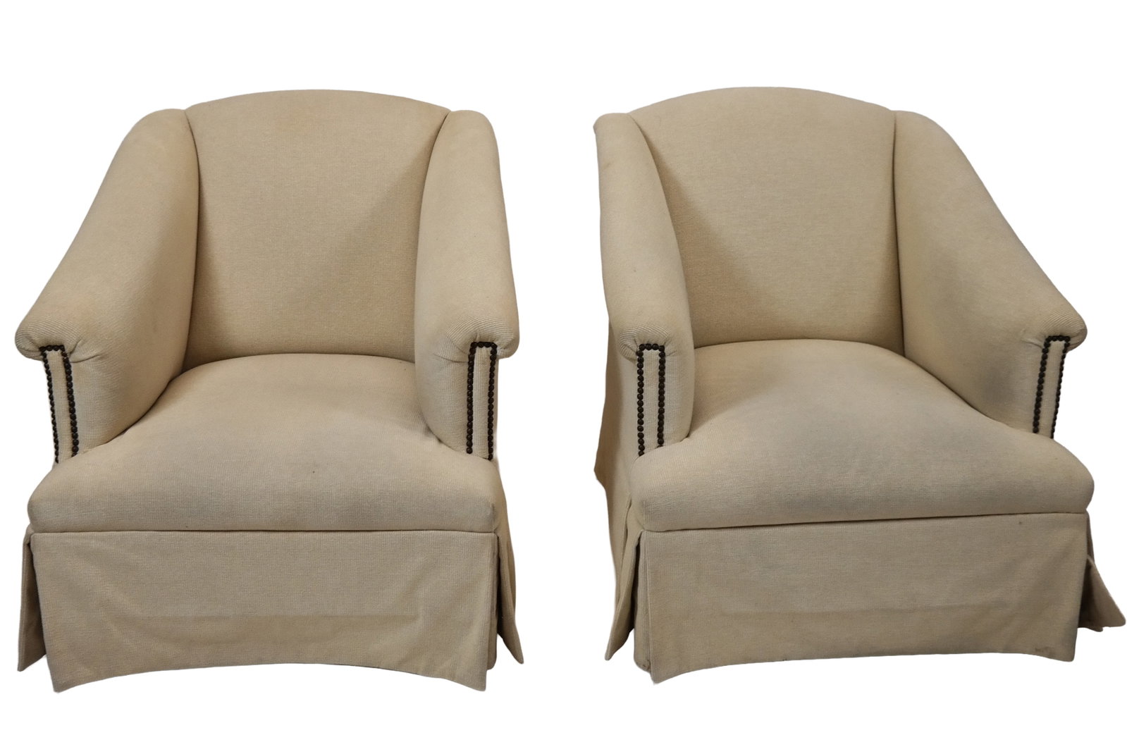 Pair Of Overstuffed Club Chairs: Pair of overstuffed club chairs, tan upholstered, with studded arm trim and skirted bases, in squared flare shapes. [34" H x 32" W x 40" D]. LOCATED ROOM 3