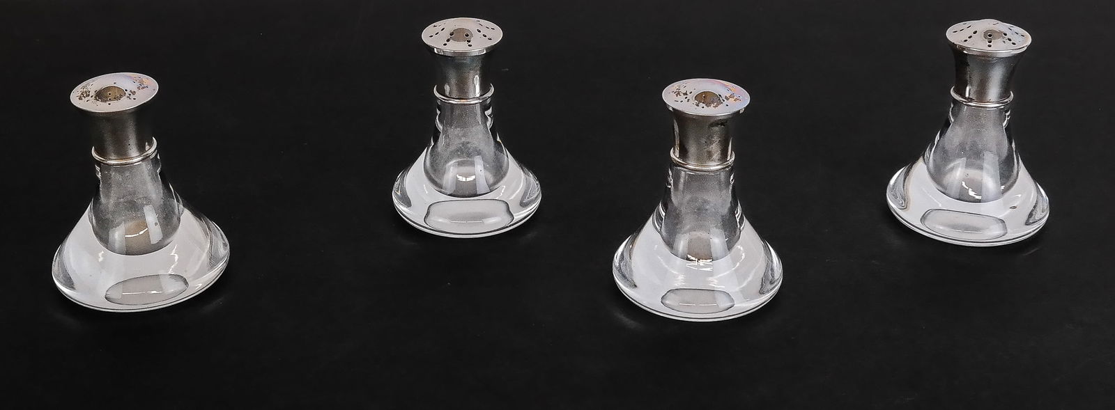 Steuben Glass & Sterling Pepper Shakers, 4: Steuben set of four crystal and sterling silver pepper shakers, marks to all bases "Steuben" and 2 silver lids "Steuben Sterling". [3.25" H x 2" Diameter]. Overall condition is good, minor spotting to