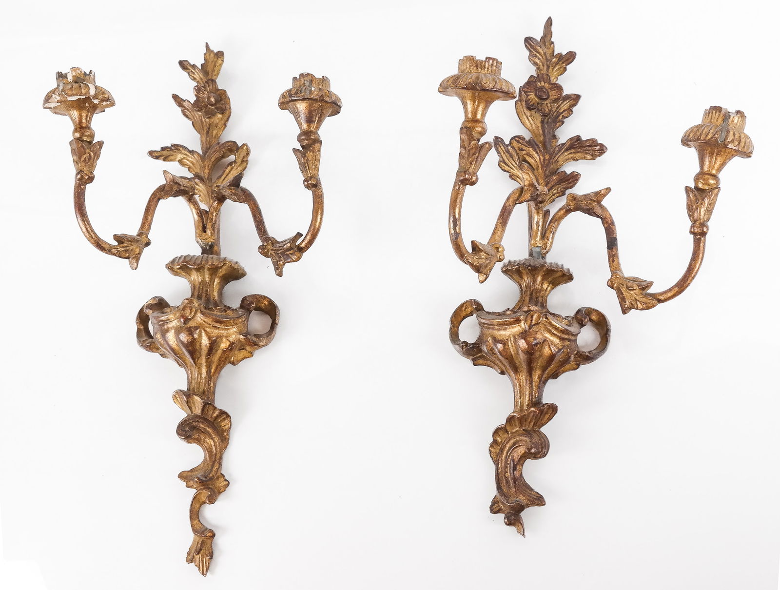 Pair Of Giltwood Cartouche Sconces: Pair of two-light giltwood sconces, floral, urn and leaf decorated, probably made in Italy. [17.5" H x 8.5" W x 7" D]. Some losses, but in overall good condition.
