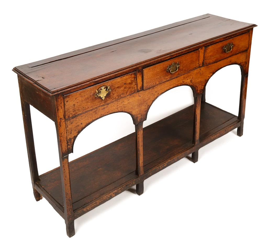 English Provincial Walnut Three-Drawer Sideboard: English Provincial walnut three-drawer console sideboard, 19th century, with brass mounted drawers to upper, over a shelf at lower with three arch decorated supports. [35" H x 62" W x 16.5" D]. Condit