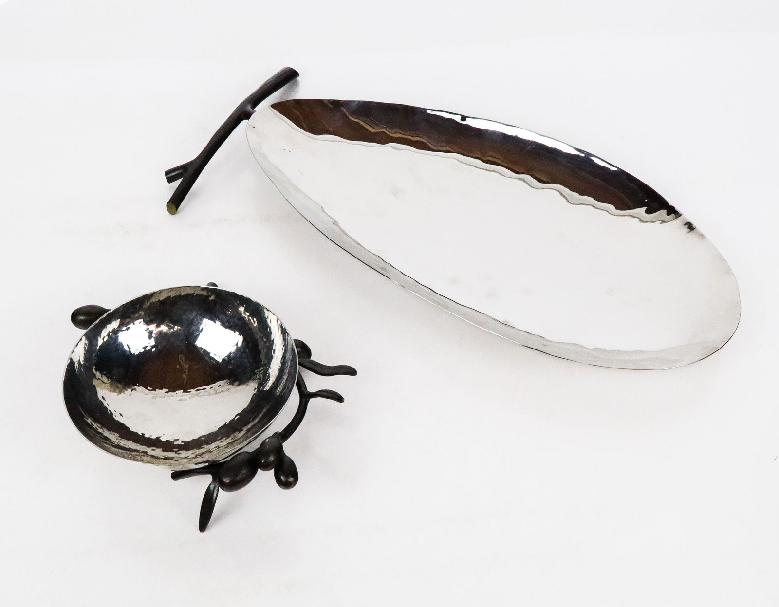 Two Michael Aram Hammered Nickel Dishes: Two hammered nickel dishes by Michael Aram, 21st century, comprising a smeller hammered dish with bronze olive mounting, and a larger hammered nickel dish with a bronze branch to one side, both signed