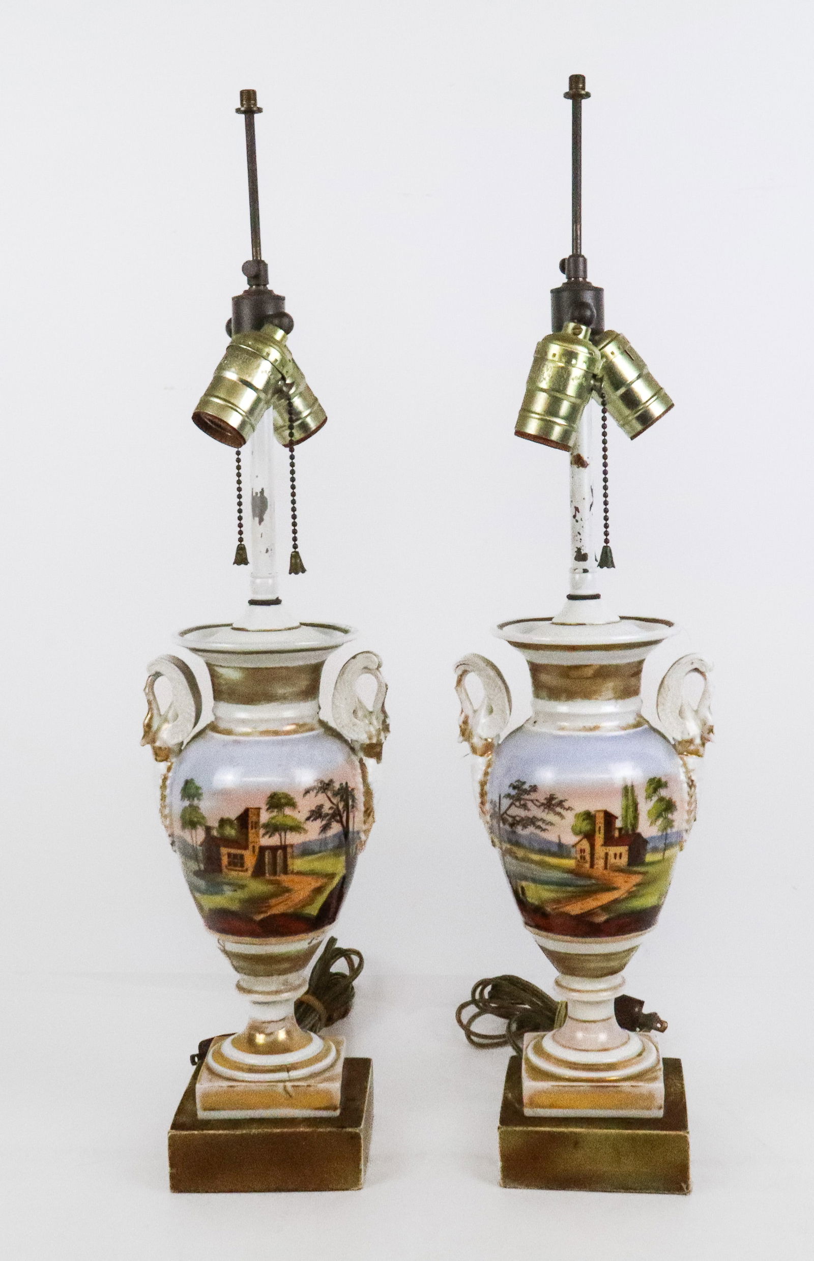 Pair Paris Porcelain Urns Mounted as Lamps: Pair of Paris porcelain hand-painted urns, 19th century, mounted as lamps with two swan form handles, hand-painted landscapes, and gilt details. [Urn: 11.5" H x 3" Square]. Condition is fair to poor w