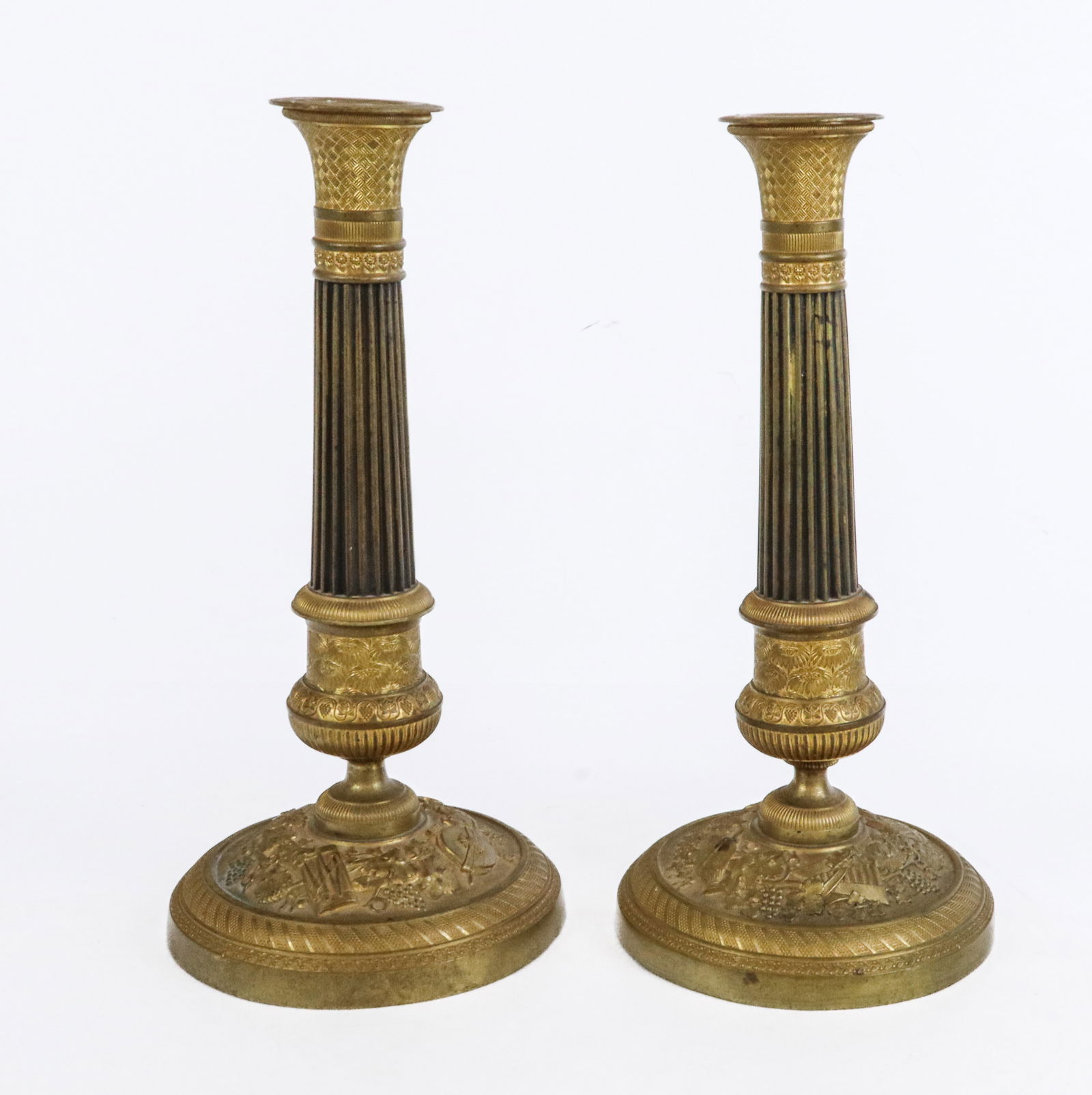 Pair of French Empire Bronze Dore Candlesticks: Pair of French Empire bronze dore and repousse candlesticks, 19th century, with etched bobeches, patinated and fluted columns, and repousse bases with grape, drum, and lute decoration in the Bacchic s