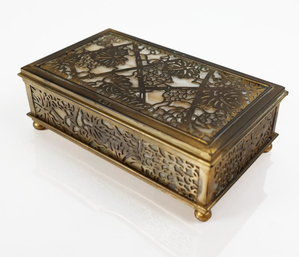 Tiffany Studio Gilt Bronze & Glass "Grapevine" Box: Tiffany Studios gilt bronze and caramel colored slag glass "Grapevine" pattern monogrammed box, New York, mark to base with inventory scratch number. [2.5" H x 6.5" W x 4" D]. Overall condition is