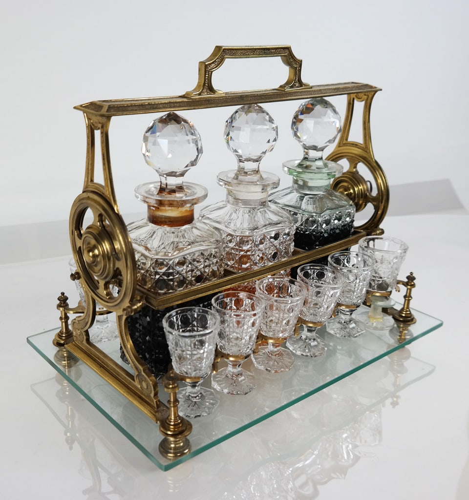 Victorian Brass, Glass and Crystal Cordial Set: Victorian brass, glass and crystal tantalus / cordial set, probably early 20th century, with three button cane patterned cut glass stoppered decanters, 12 cordials en suite, and a locking hinged