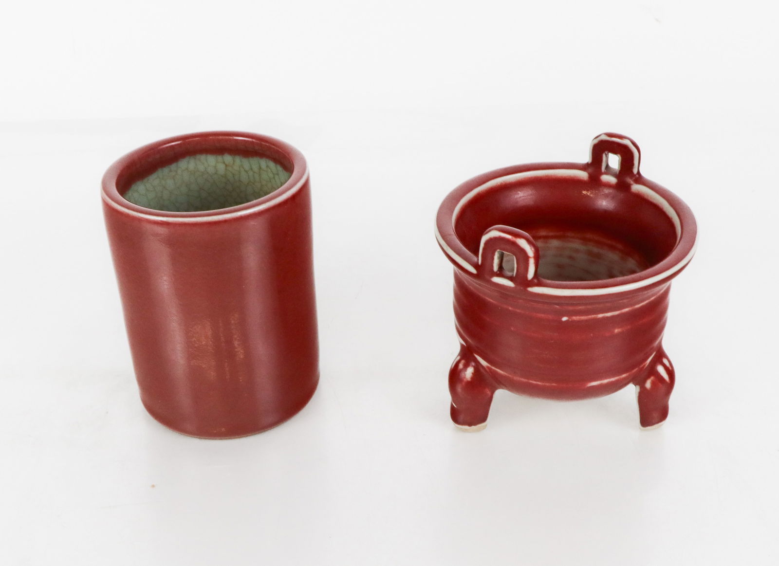 Chinese Sang de Boeuf Porcelain Articles, 2: Two articles of Chinese oxblood sang de boef porcelain, 20th century, comprising a brush pot with celadon glaze to interior, and a porcelain vessel in the form of a two-handled ding, each unmarked.