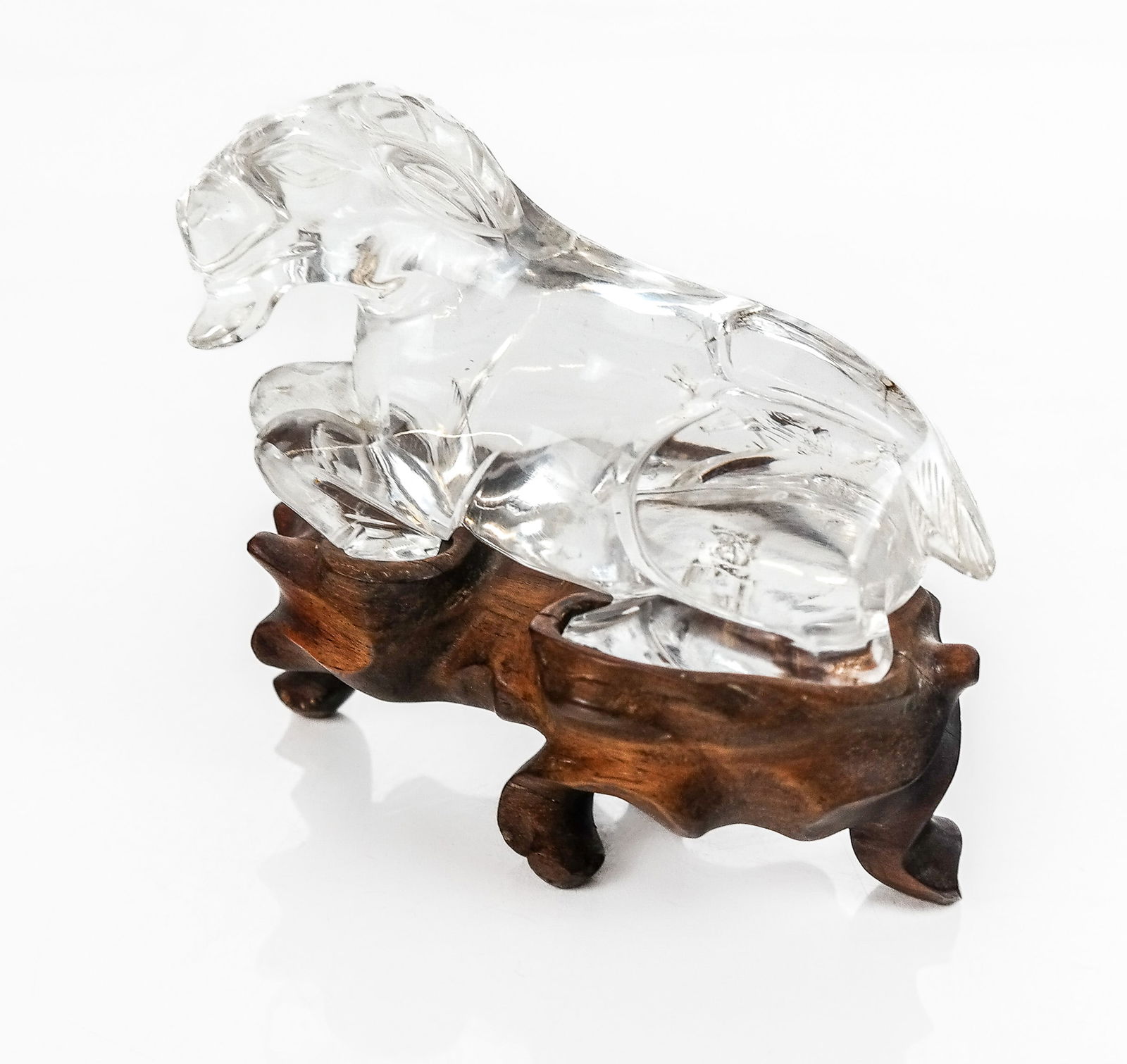 Chinese Carved Rock Crystal Goat on Stand: Chinese carved rock crystal goat, 20th century, on a carved wood stand. [Less stand: 2.5" H x 4.75" W x 2.5" D]. Condition is good. From the Collection of Sonia and Philip Reine of Long Island.