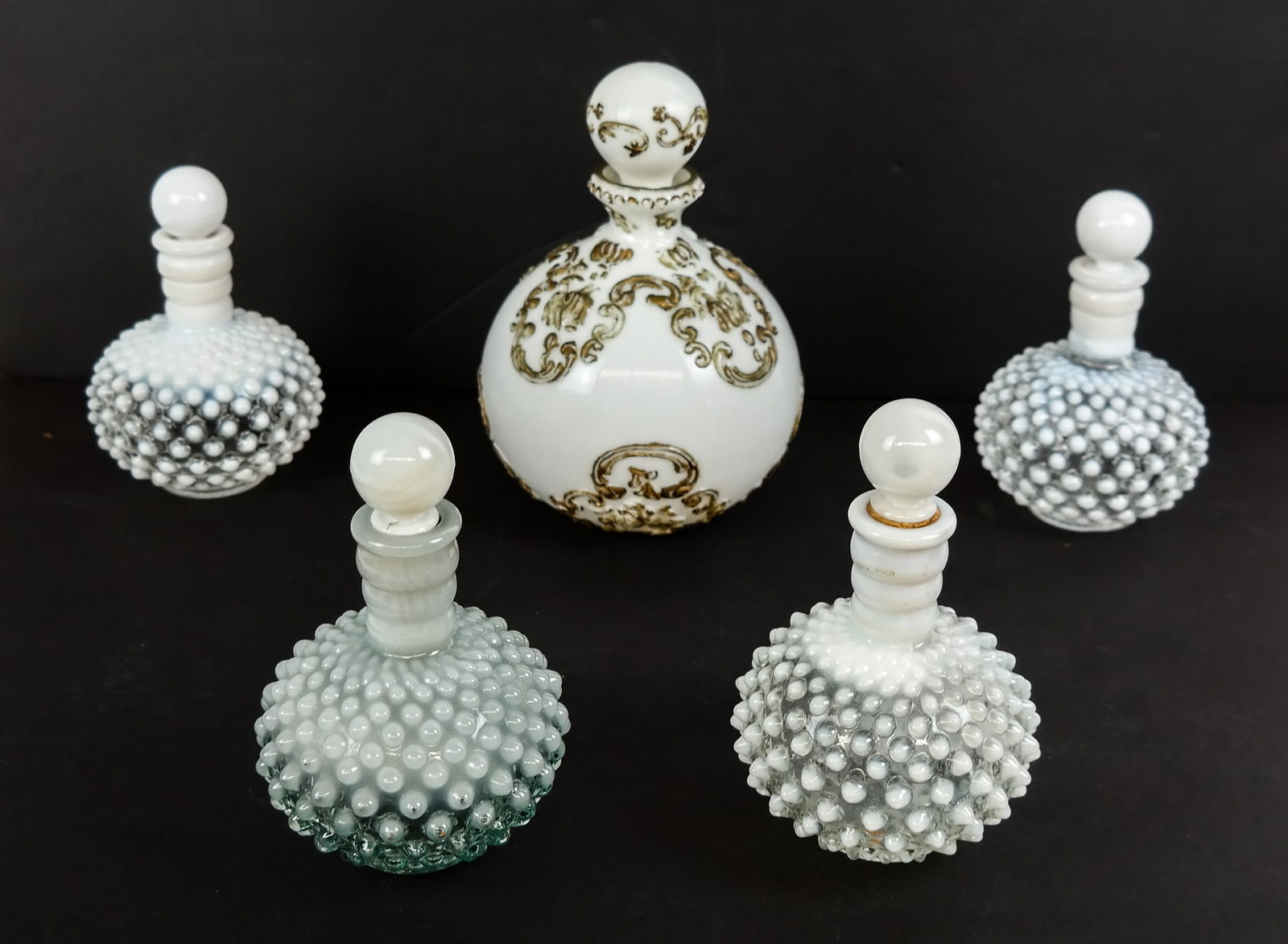 4 Hobnail Glass Perfume Bottles & 1 Other, 5: Vanity group, 20th century, including a set of four clear-to-white hobnail glass perfume bottles and stoppers, together with a Victorian style milk glass decanter/vanity bottle with raised scrollwork
