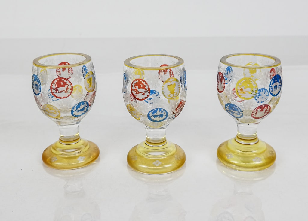 Set of Three Bohemian Cut to Clear Cordials: Set of three Bohemian cut to clear cordials, Austria/Bohemia, 19th century, with red, yellow, and blue cut to clear cartouches with animal architectural and nautical scenes, and floral etched