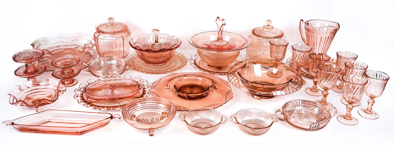 Collection of Rose Colored Depression Glass, 34: Collection of rose colored depression glass, early-mid 20th century, comprising 8 stemmed glasses, 16 bowls and serving trays, 3 plates, a handled pitcher, 2 biscuit jars, and 4 candlesticks. Stems