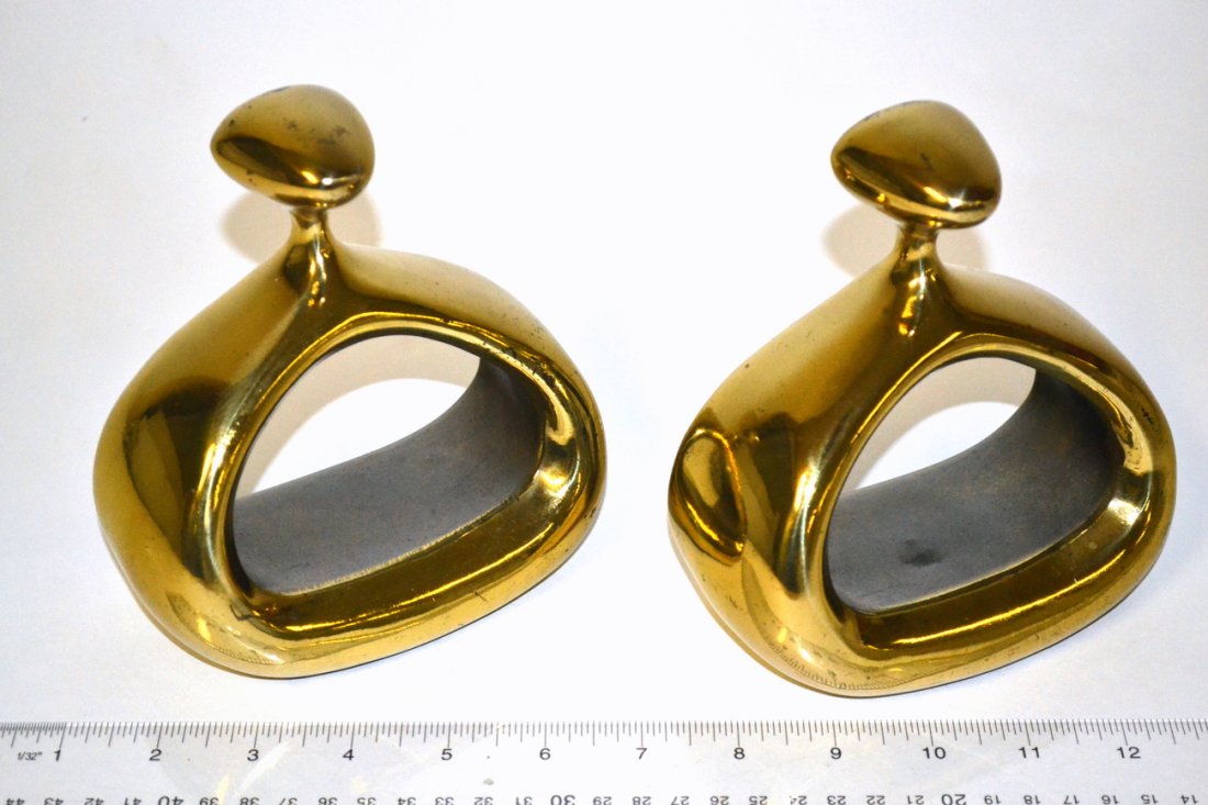 Pair of Ben Seibel Bookends for Jen-Fred Ware: Brass finish stirrup-form modern bookends. Each bear partial Jen-Fred ware labels on bottom over original felt. Both signed "Jen-Fred" in the metal on back. [5 3/8" W x 2 7/8" D x 5 5/8" H]. Finish wo