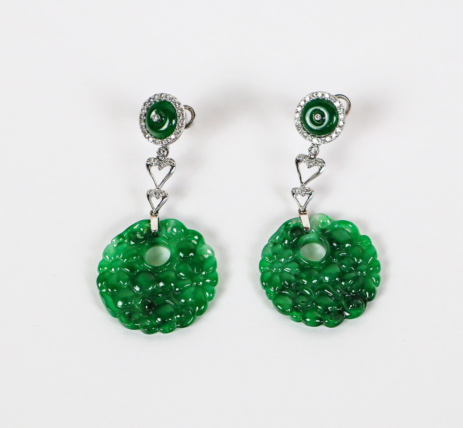 Pair of Jadeite Jade and Diamond Ear Pendants: Pair of jadeite jade, diamond and 18K white gold ear pendants, designed as jade buttons accented with center and border of diamonds continuing to heart shaped links suspending delicately foliate