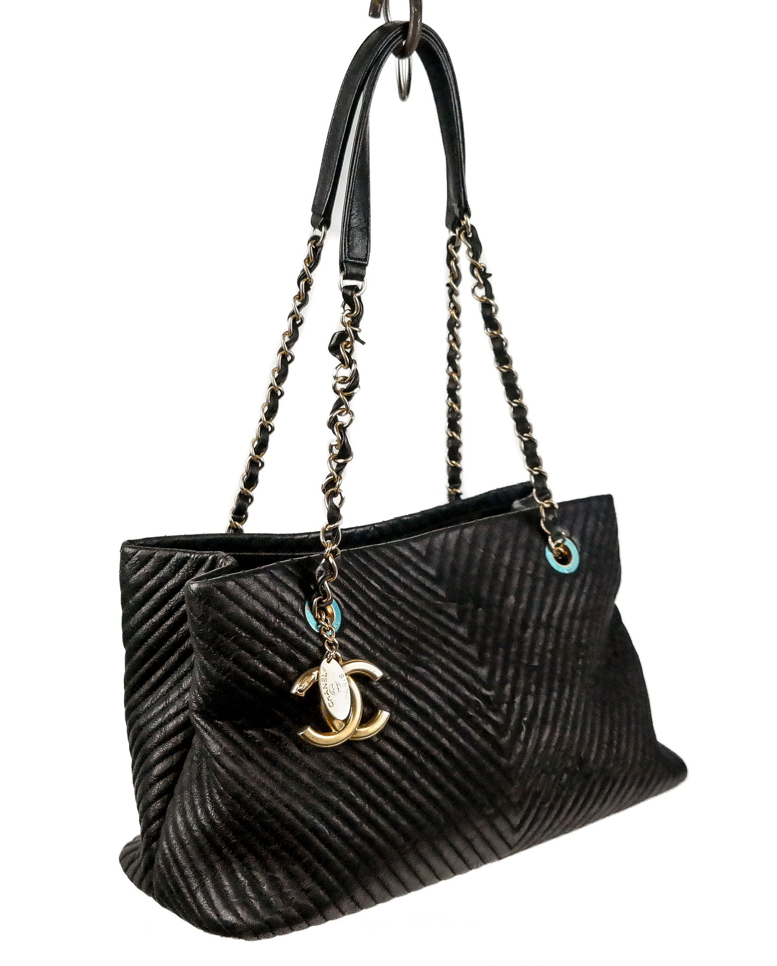 Chanel Surpique Chevron Leather Tote Bag: Chanel Surpique chevron leather tote in black, from the 2015 collection by Karl Lagerfeld, having gold-toned hardware with chain-link shoulder straps, maroon canvas lining, and CC charm, hardware mark