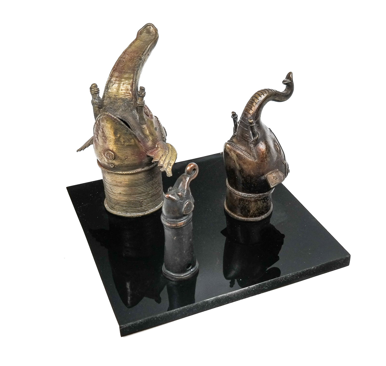 Three Bronze Elephant Heads on Stand: Group of three bronze elephant heads on stand, the heads are Palanquin Handles of brass and other metals, 19th Century, on custom fitted acrylic stand. [10" H x 12" Square]. Medium head has break and