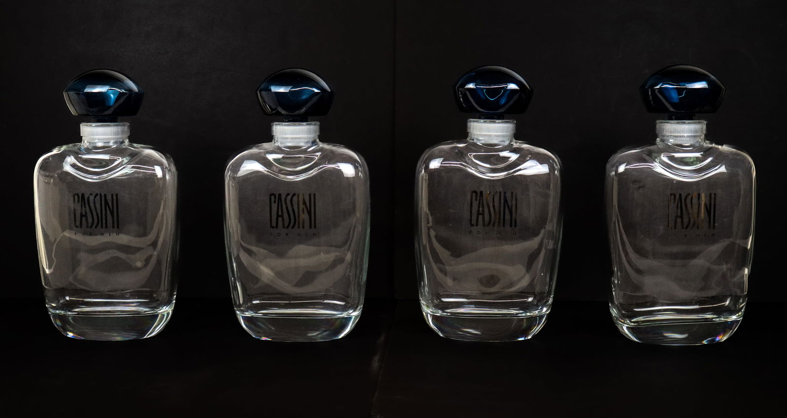 Oleg Cassini Set of Four Large Decorative Decanter: Oleg Cassini set of four blue and colorless glass decanters modeled after Cassini fragrance Por Homme. [ 13" H x 7" W x 3" D]. Overall condition is good.