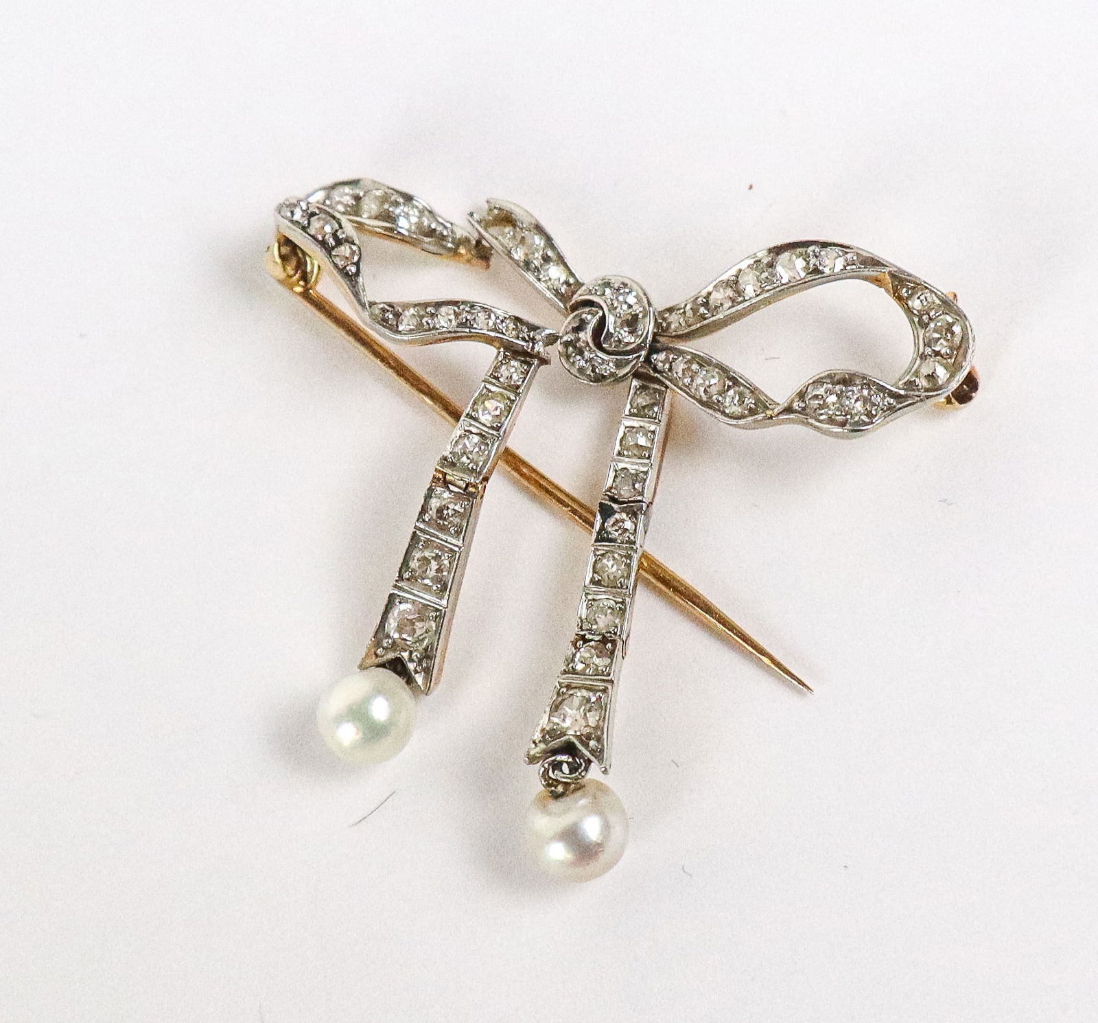Gattle Platinum, Gold, Diamond and Pearl Brooch: Gattle antique millegrained platinum top yellow gold, diamond and pearl bow brooch with pearl drops, marked "Gattle" on pin stem, tests for 14K gold and platinum. [4.15 dwt., 1.5" Square]. Overall con