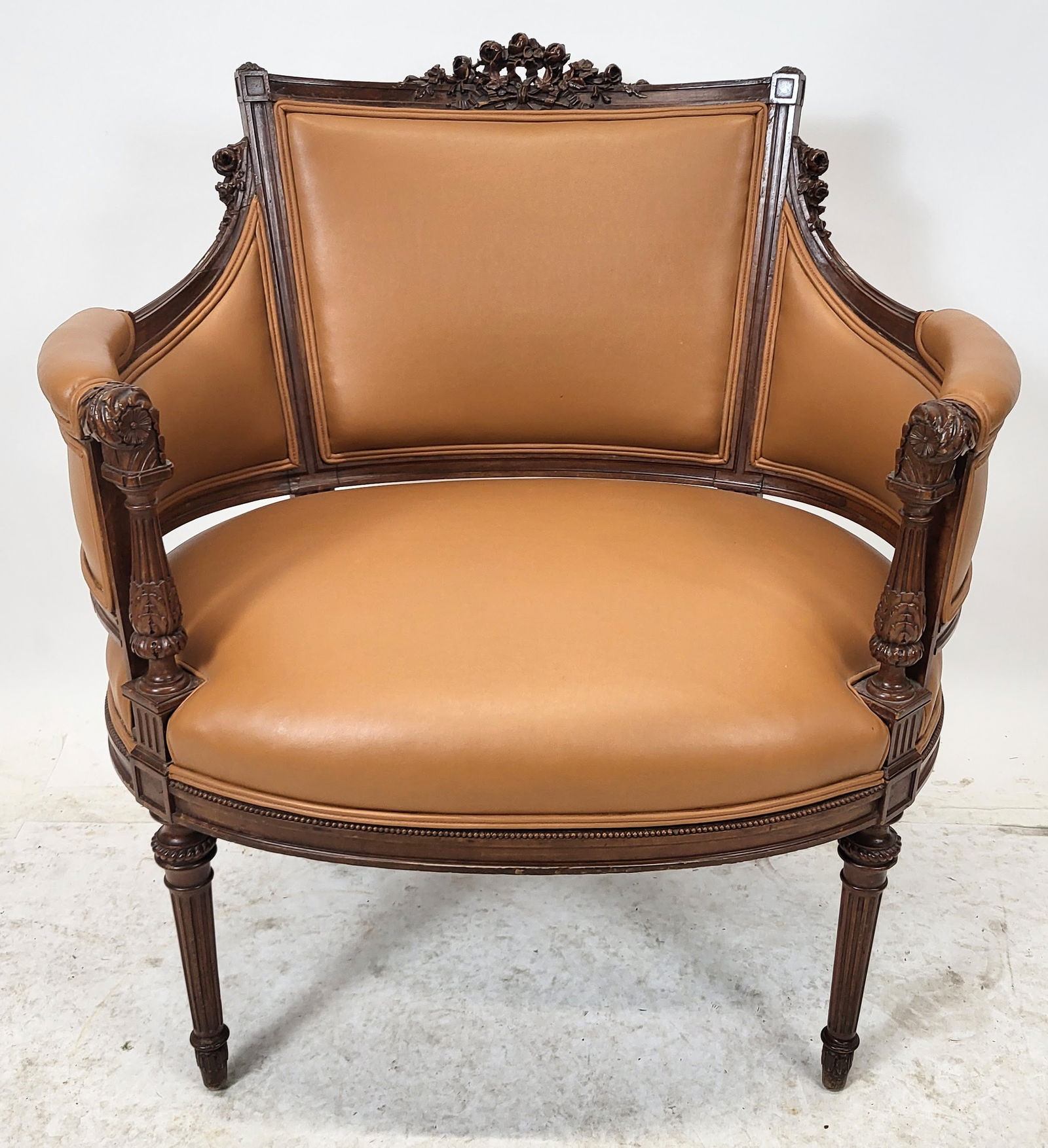 Louis XVI Faux Leather Upholstered Marquise: Louis XVI faux leather upholstered marquis, floral carved crest rail and ears, pad arms above a roundabout frame, fluted legs. Similar to previous lot. [35" H x 32" W x 25" D]. Very good condition.