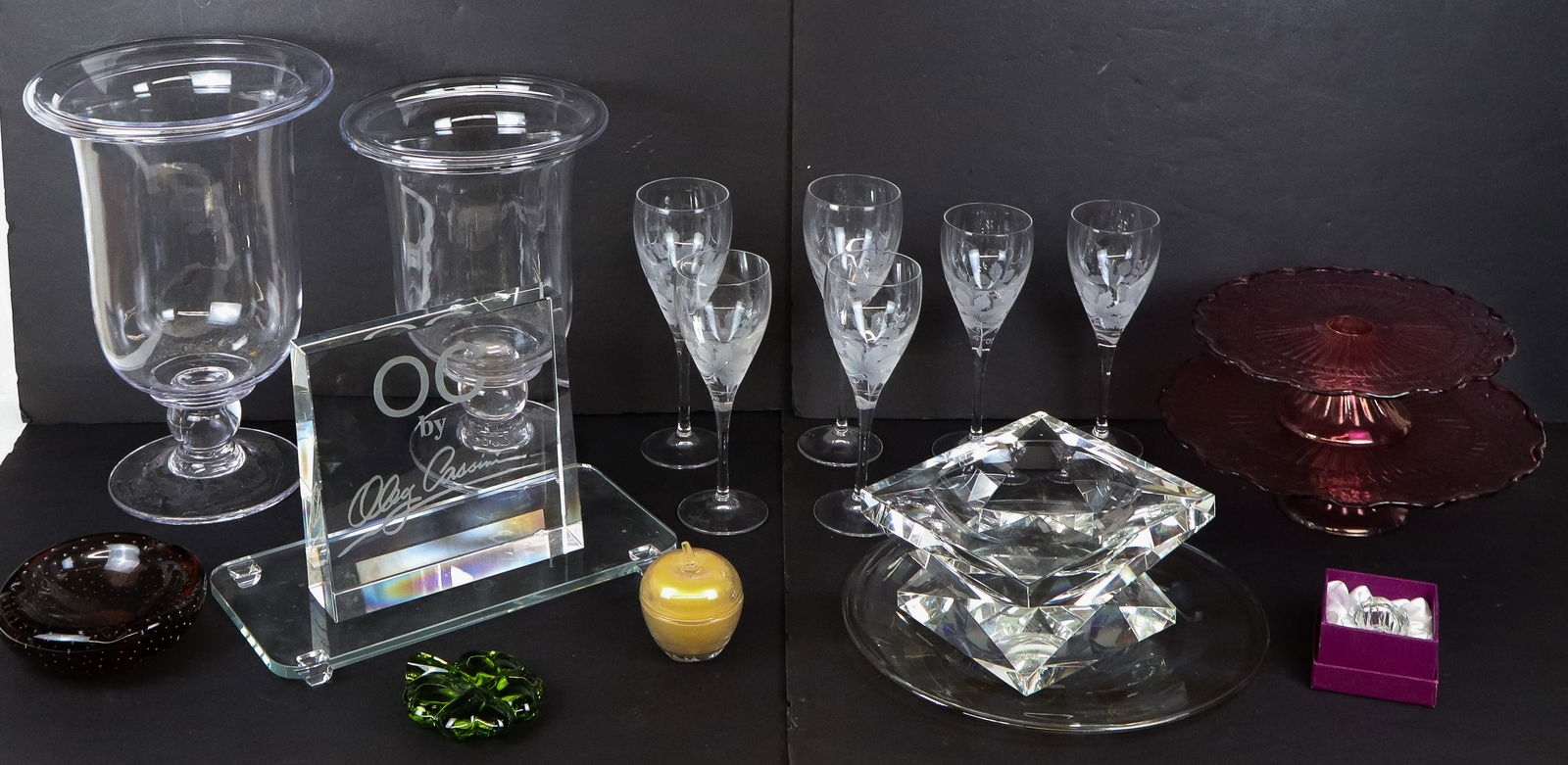 Assorted Glass Decorations and Articles (16+): 2 Oleg Cassini square blocks, Oleg Cassini coupe, glasses, 2 hurricane vases, Italian bowl, Shamrock, Oleg tray, 2 colored glass coupes, etc.[Tall vase 14" H x 9" diameter]. Good condition, coupe has