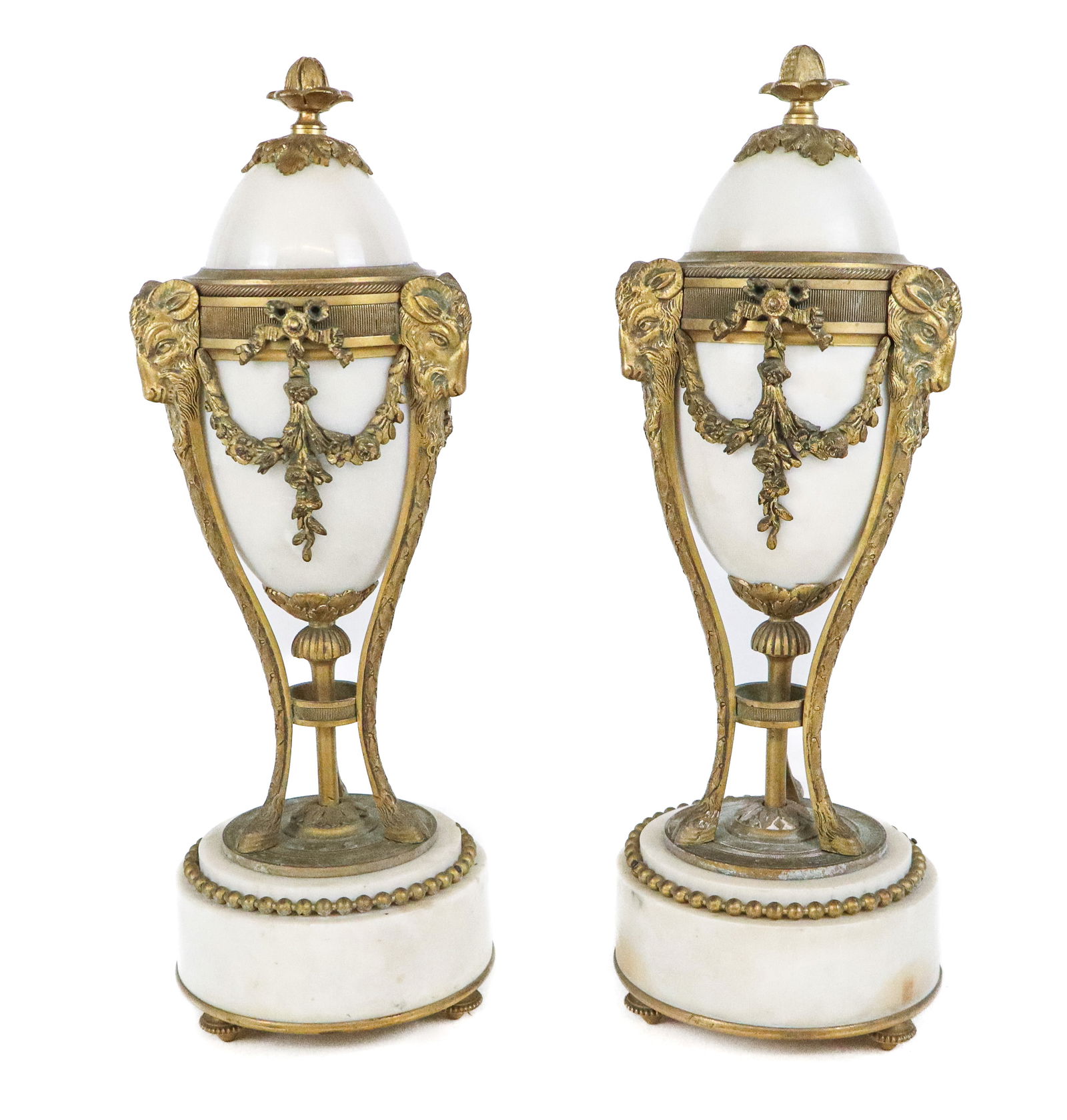 Louis XVI Bronze & White Marble Cassolettes, Pair: Pair of Louis XVI marble and bronze dore cassolettes, 19th century, with removable lids which convert to candle holders, supported by goat head and floral swag decorated gilt bronze supports, terminat