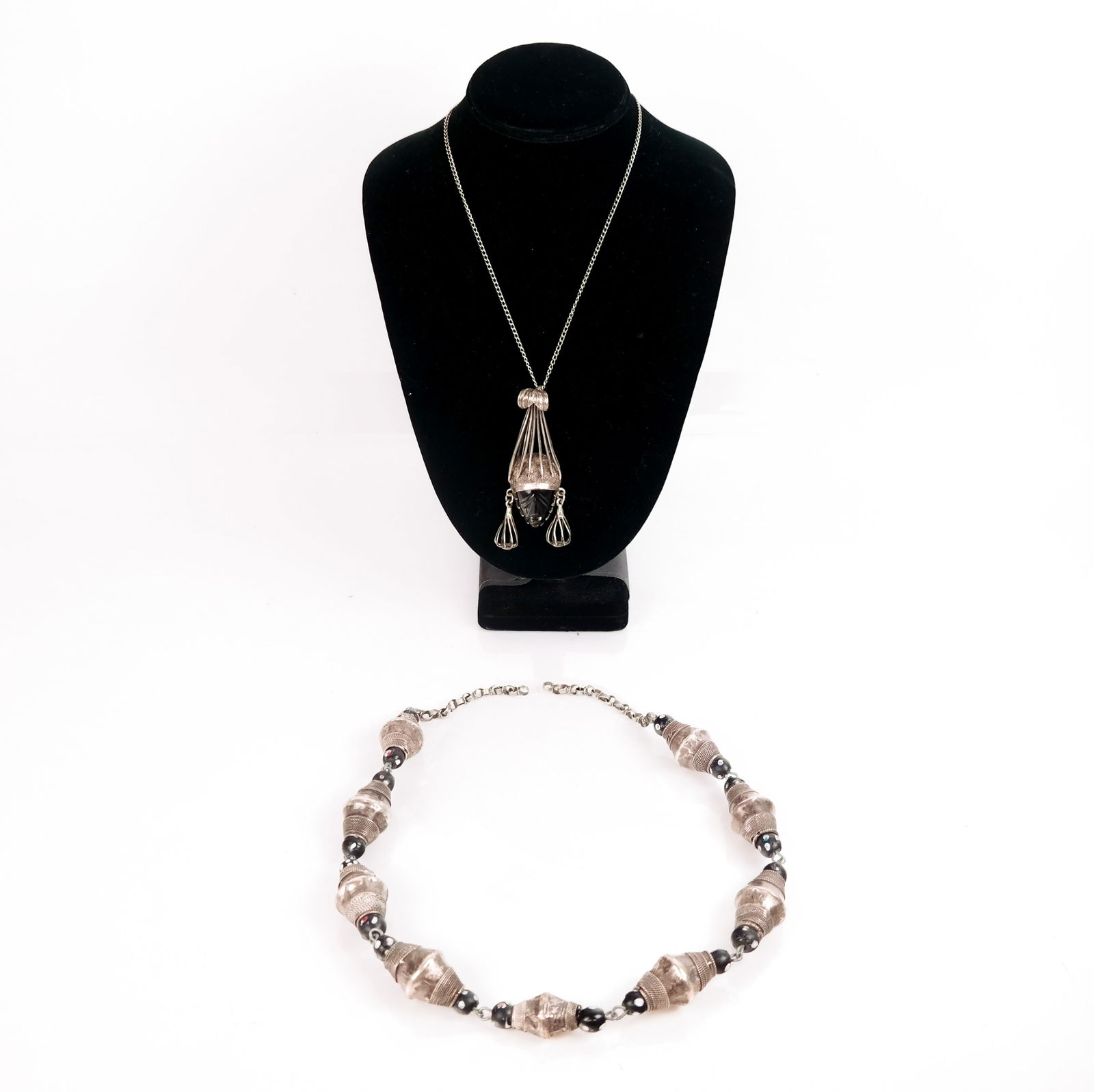 Two Silver and Silver-Mounted Necklaces: Mexican silver facial-mounted pendant (Taxco) on a metal chain necklace [Pendant: 3.5" H] and a beaded mounted silver conical-form necklace [26" L, overall]. Condition reports and requests for additio