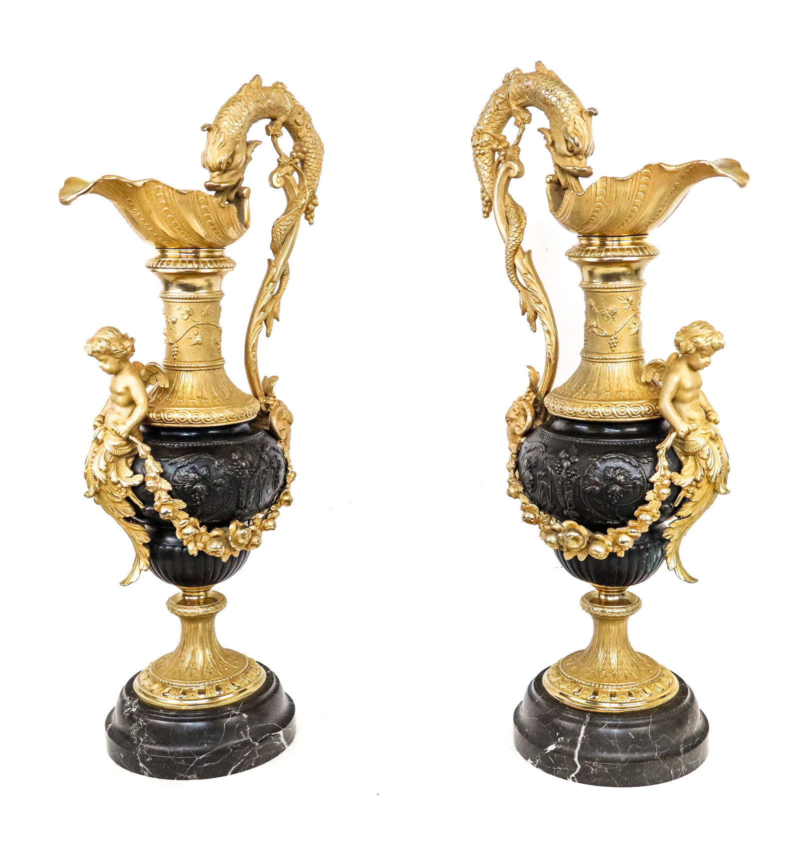 French Empire Bronze Ewers, Pair: Pair French Empire bronze faux ewers, the shell shaped spout with a sea serpent handle wrapped in grapevine and ending in a rams head, the front with a cherub mount, in dore bronze, a patina bronze bo