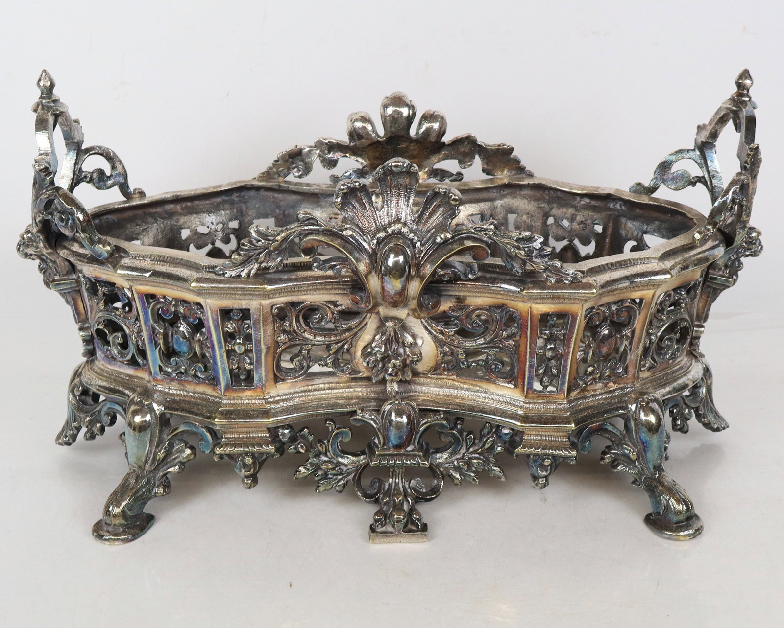 French Silvered Metal Centerpiece Bowl: French silvered metal centerpiece bowl with scrolls and high open handles, in oval form, with large gothic style legs. [11" x 20" x 10"]. Bottom bent and loose, one handle apparatus loose.