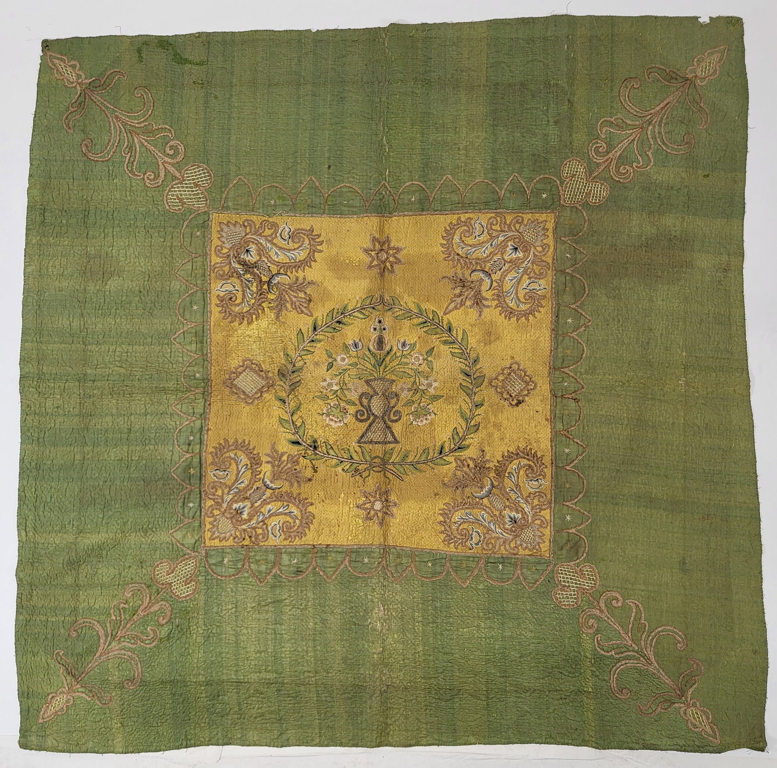 18th C. French Silk Embroidered Boutis Quilt: An 18th Century French boutis quilt with cotton wadding having silk thread, chenille, and silver embroidery on a yellow quilted silk center with an urn of flowers surrounded by laurel leaves and corne