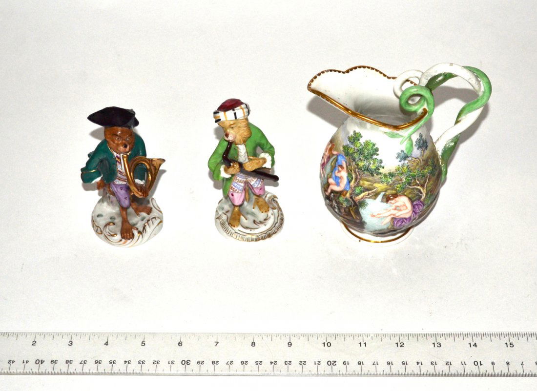 Continental Porcelain Lot: Comprises two Dresden monkey musicians (oboe and French horn players) and an erotic Capodimonte petit pitcher. Monkeys [4 3/4" H] in good condition. Pitcher [6" H] with repaired handle.