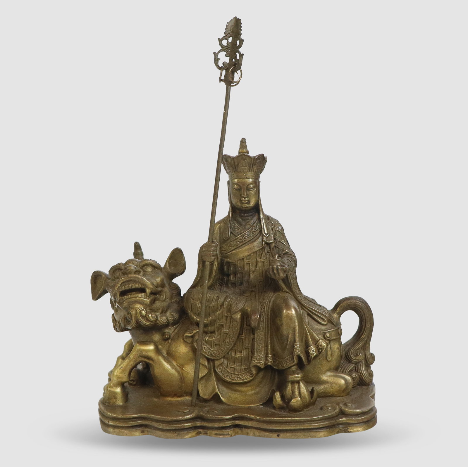 Bronze Figure of Ksitigarbha: Bronze figure of Ksitigarbha, 20th century, seated atop a foo dog, and holding a staff, unmarked. [7.5" H x 5" W x 3" D]. Condition is good.