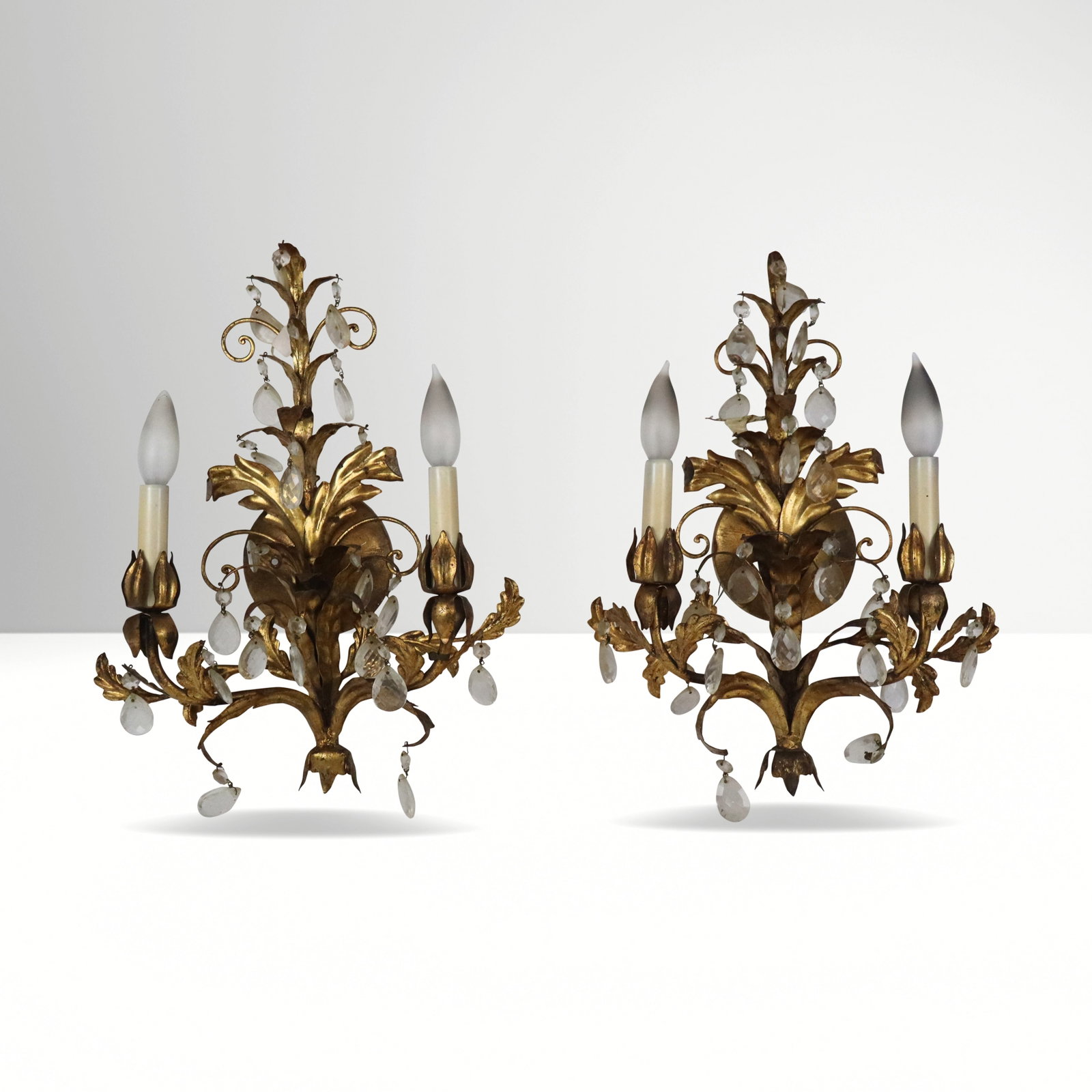 Pair of Gilt Metal Foliate Sconces: Pair of gilt metal and crystal pendant two light wall sconces, 20th century. [17" H x 14" W x 6.5" D]. Overall condition is fair, require rewiring, some loss to gilding and pendants.