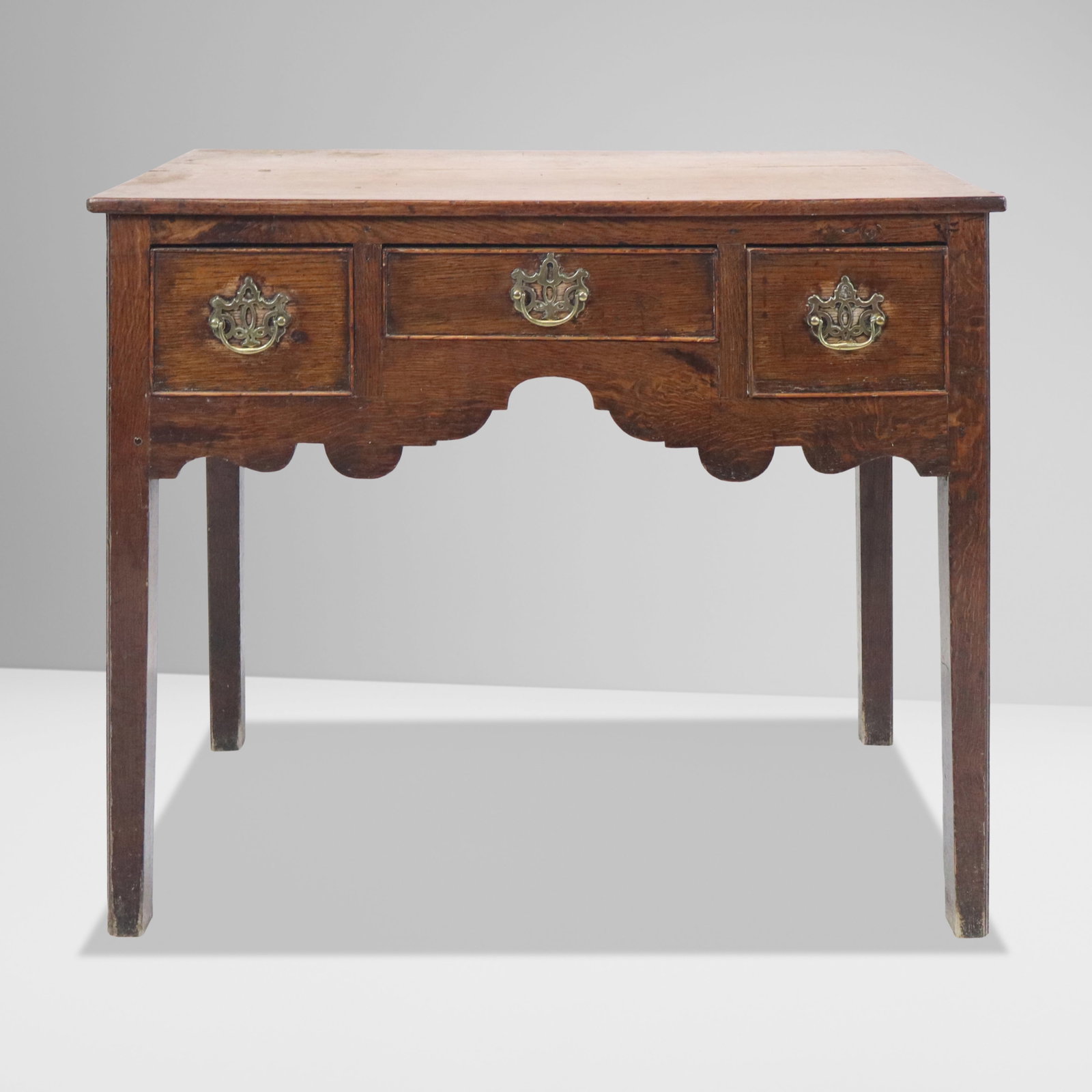 Georgian Oak Lowboy: Georgian oak lowboy, 18th century, with three brass mounted drawers and decorated apron to lower. [28" H x 32" W x 18" D]. Condition is good with age-commensurate surface wear.
