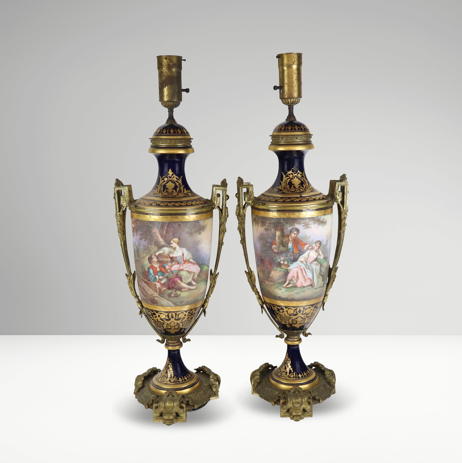 Sevres Pair of Louis Philippe Porcelain Urns Mount: Pair of Sevres hand-painted porcelain and gilt bronze vases mounted as lamps, French, probably 20th century, of urn form, the tops and bases with cobalt blue ground and gilt decoration centering river