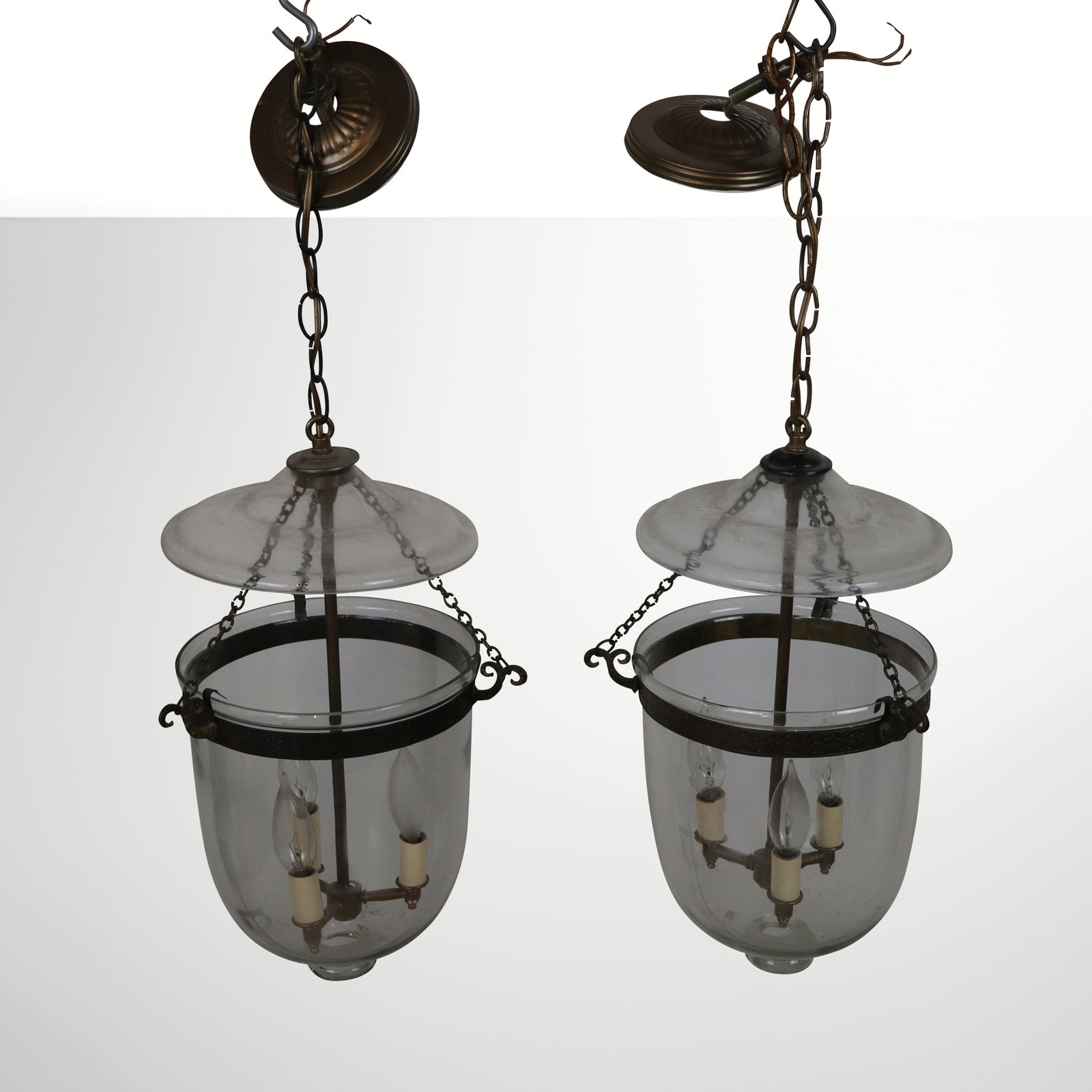 Pair of Vaughan Glass and Brass Bell Chandeliers: Pair of Vaughan bell chandeliers, 20th century, with pressed brass and hand-blown glass and phoenix form chain supports, unmarked. [Fixture: 21" H x 11" Diameter]. Condition is good with a minor chips