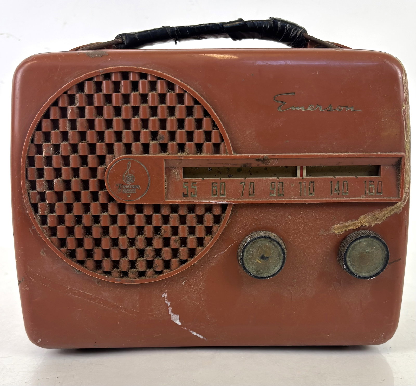 Emerson 646 Bakelite 1950s Radio: Emerson 646 Bakelite radio, 1950s, the lunchbox design featuring a checkered grille. [7" H x 8.5" W x 4" D]. Damages, wear, residue, handle broken and taped, body with losses and cracks, not in workin