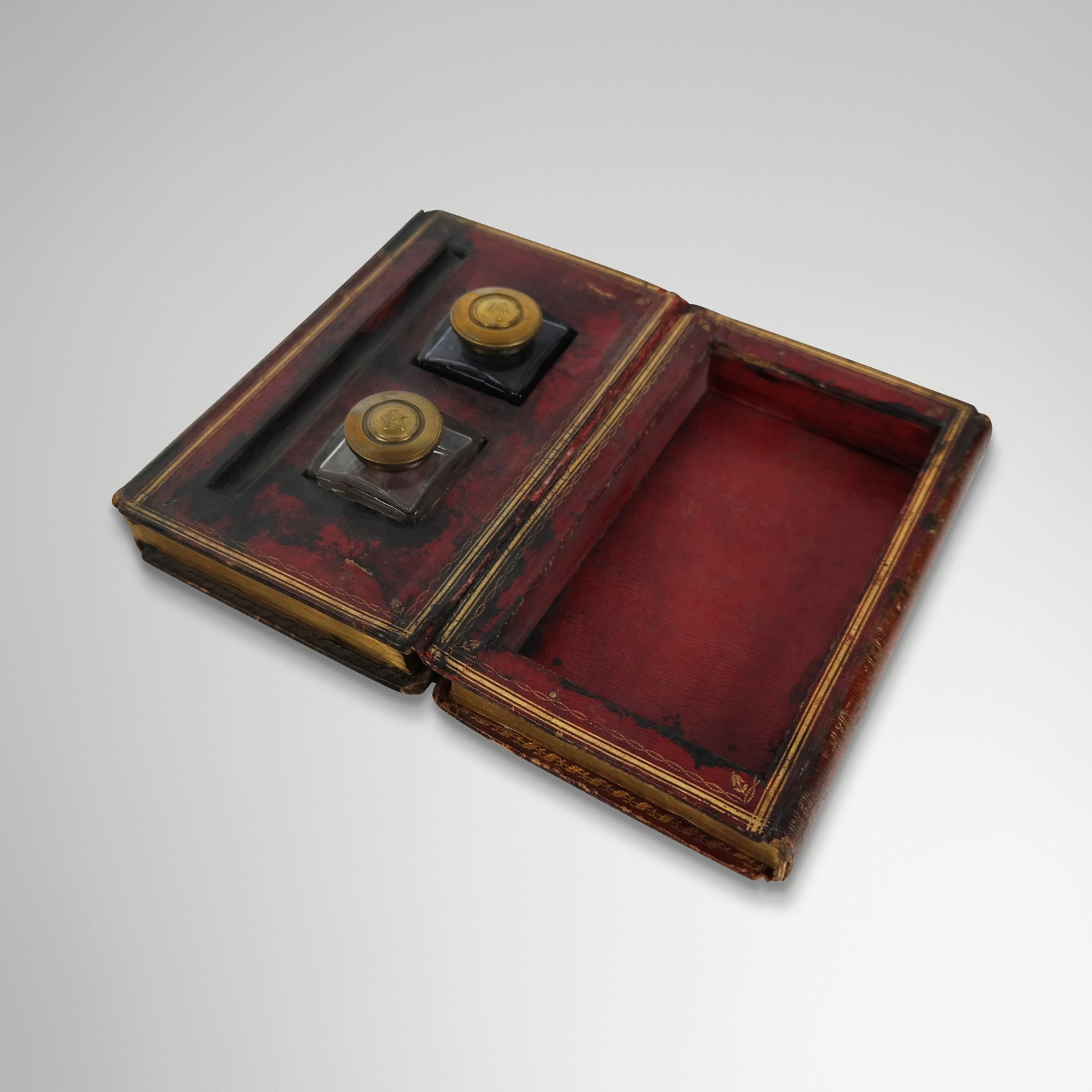 Regency Tooled Leather Book Form Inkwell: Regency tooled leather inkwell, later 19th century, in the form of two leatherbound books, opening to reveal a double inkwell with pen tray. [2.75" H x 8.75" W x 6" D]. Condition is good with wear to 