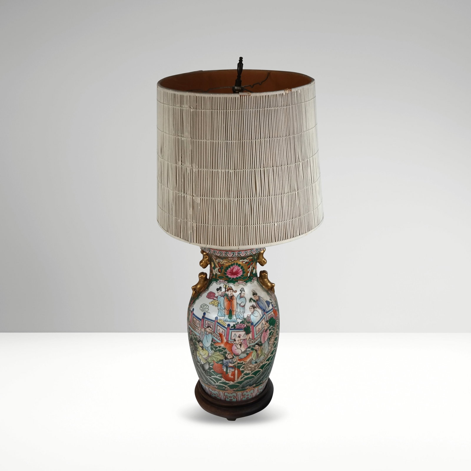 Chinese Export Vase as a Lamp with Figures: Chinese export vase, 20th century, with figural, gilt, and architectural decoration, mounted as a lamp on a wooden base with a shade. [Lamp, to lip: 16" H x 7" Diameter]. Condition is good, wiring unt