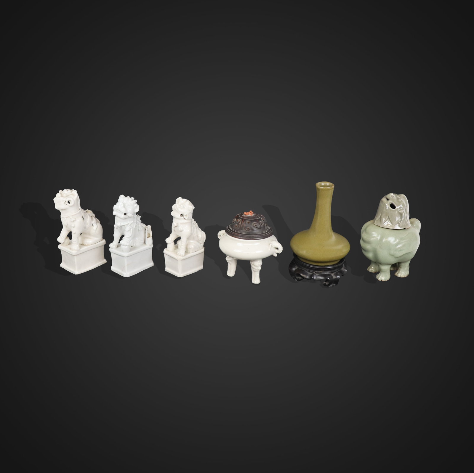 Six Assorted Chinese Porcelain Articles: comprising a Chinese tea-dust glazed vase on a wooden stand, a pair and another blanc de chine foo dogs, a porcelain ding with carved wood lid and coral finial, marked to base, and a celadon glazed ce
