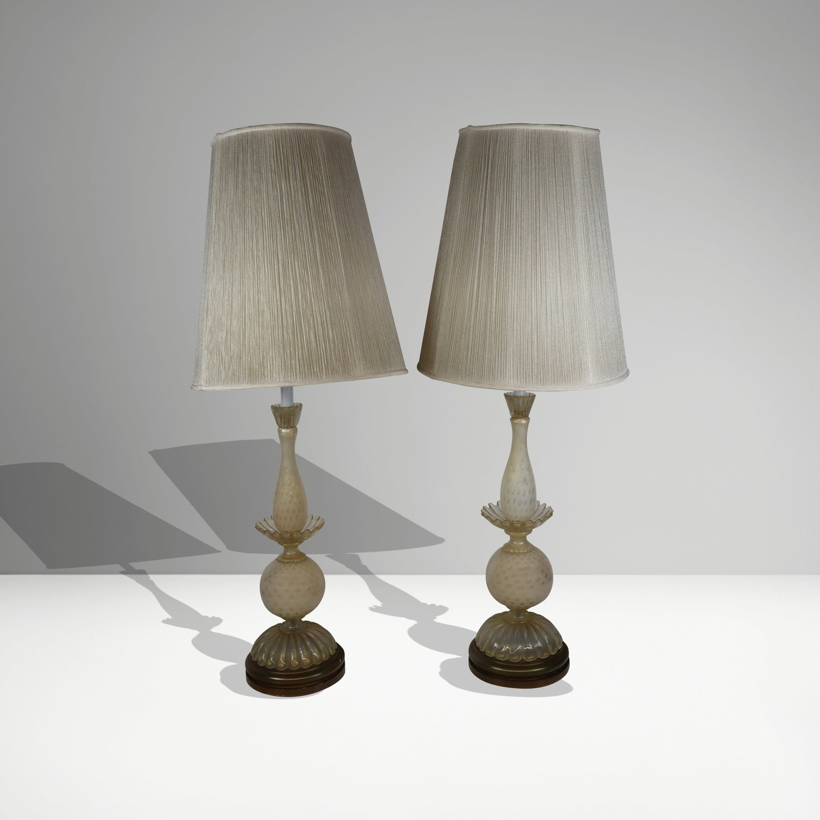 Pair of Mid-Century Murano Glass Lamps: Pair of Murano glass mid-century lamps, Italy, with avventurina and bubble accents, mounted on gilt bases, and each with a string shade. [Lamp, less shade, to socket: 30" H x 8.5" Diameter]. Condition