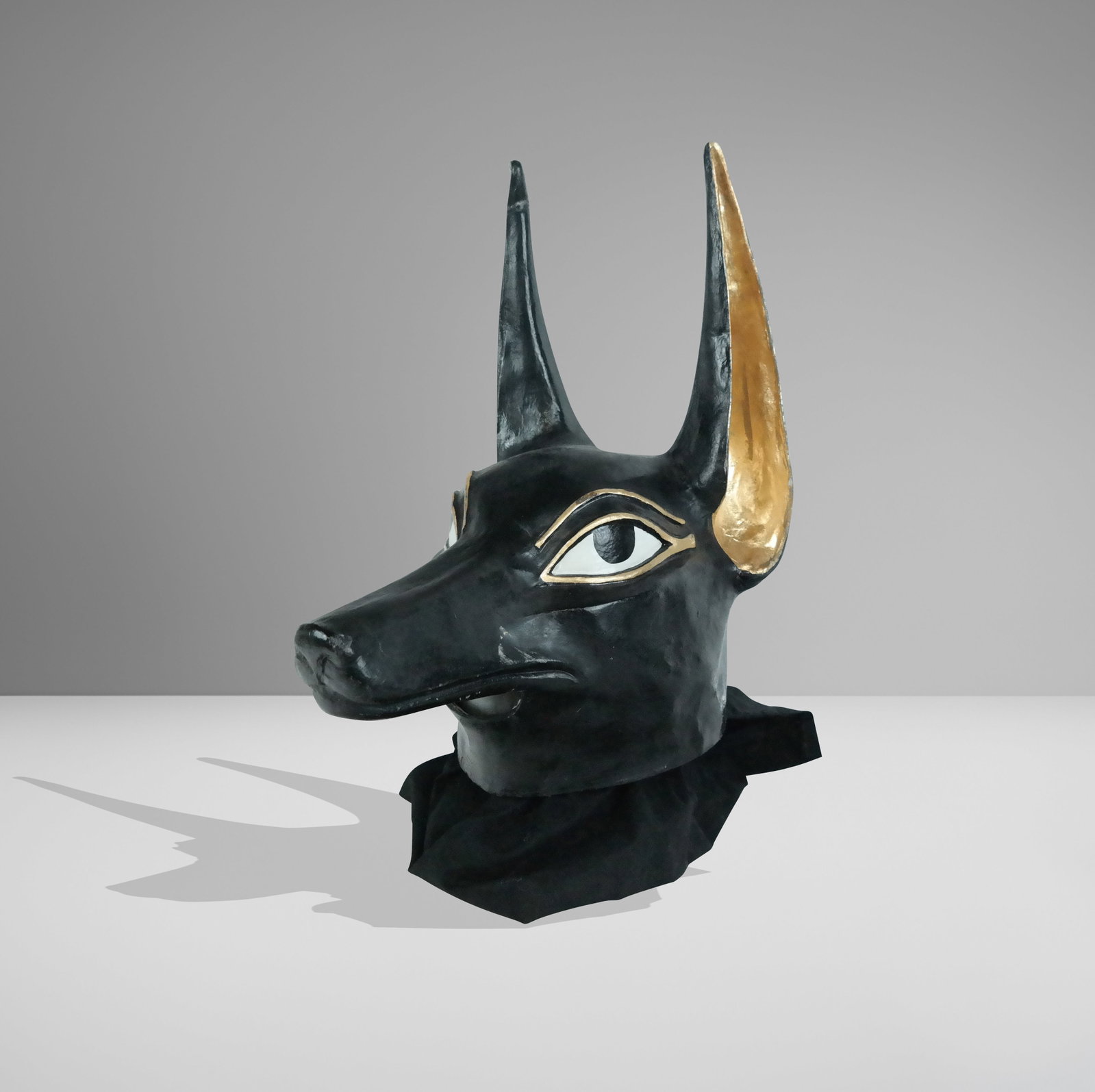 Papier Mache Mask of Anubis: Papier mache mask of Anubis, likely Venetian, with hand-painted and gilt details, and an affixed fabric collar to lower, unmarked. [17" H x 12" W x 16" D]. Condition is good with a repair to one ear. 