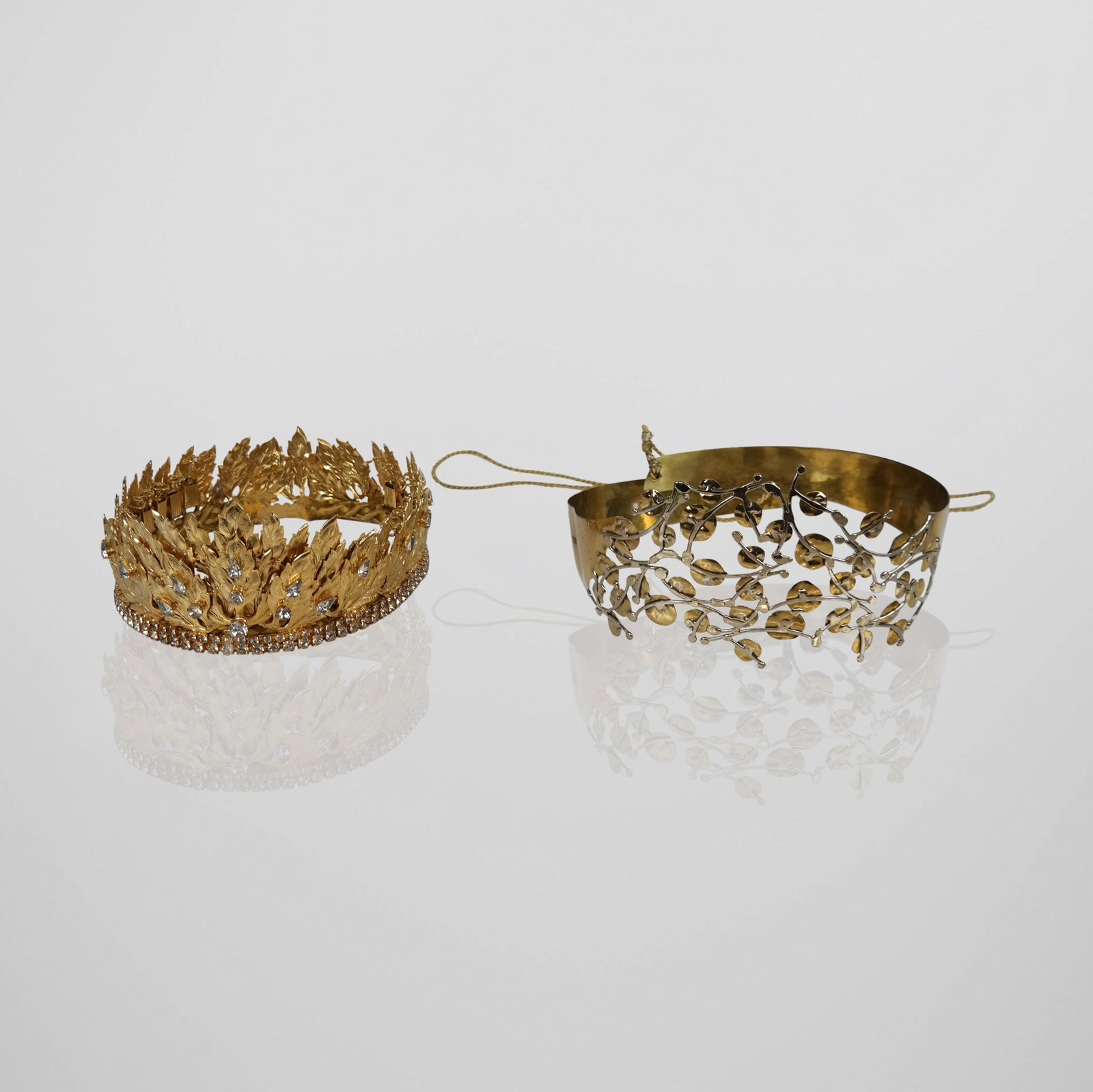 Two Crowns: Two crowns comprising a gilt and silvered metal crown with foliate design, and a gilt metal crown with inset rhinestones. [Larger: 5" H x 9" W x 10" deep; interior circumference adjustable; smaller: 4