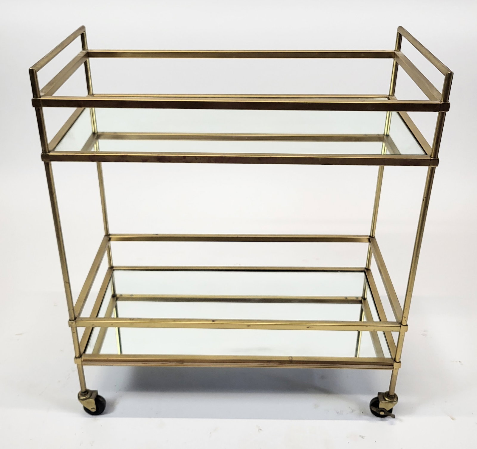 Modern Brassed Two Tier Rolling Serving Cart: Modern brass plated two tier rolling serving cart, American late 20th century, with 2 inset glass shelves and galleries, locking wheels. [30" H x 28" W x 14" D]. Good condition.