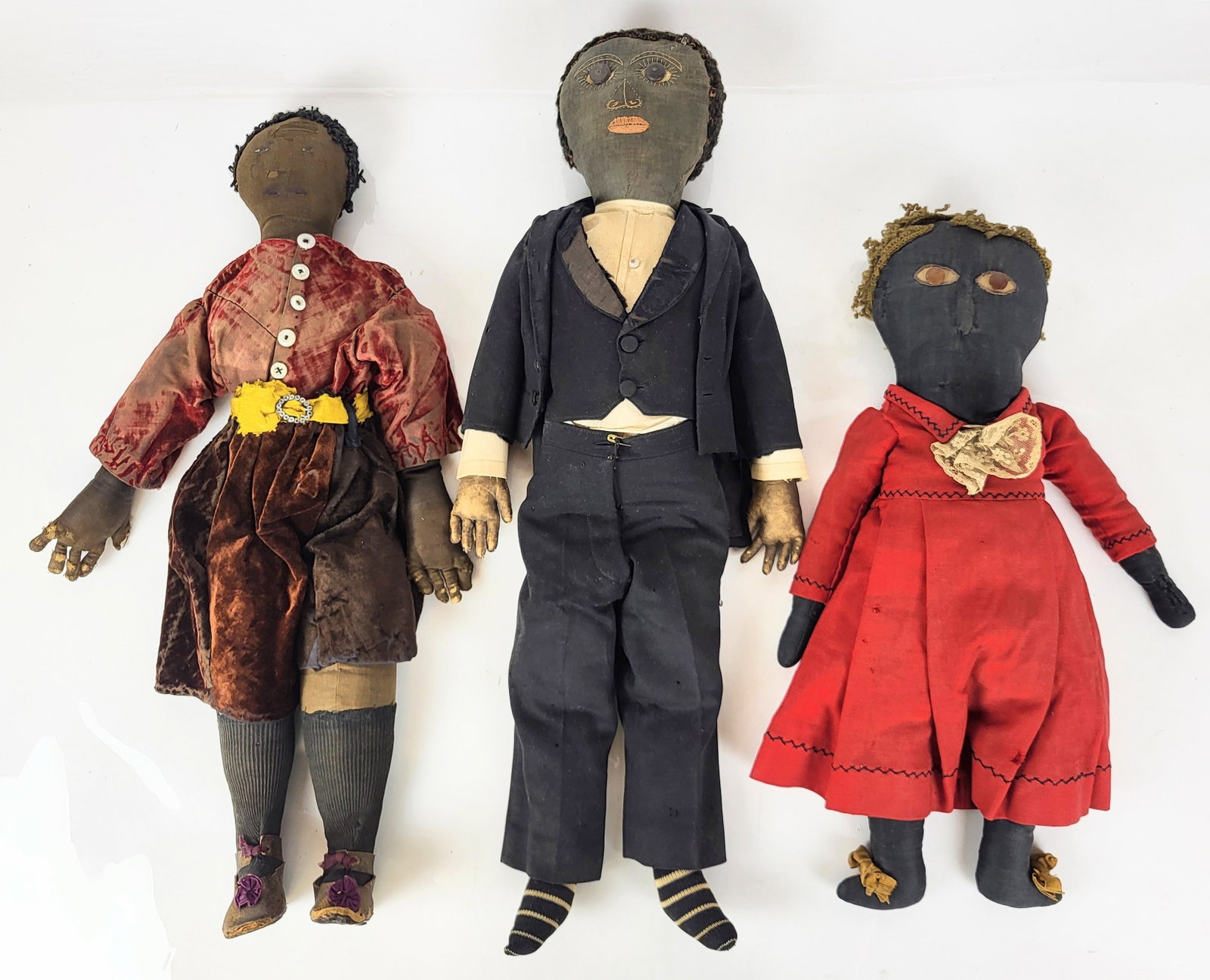 Black Americana Three Folk Art Rag Dolls: Three Black Americana Folk Art rag dolls, 19th/early 20th century, comprising a doll in velvet garb with mother-of-pearl buttons, leather shoes, and a rhinestone belt buckle, a doll with button eyes