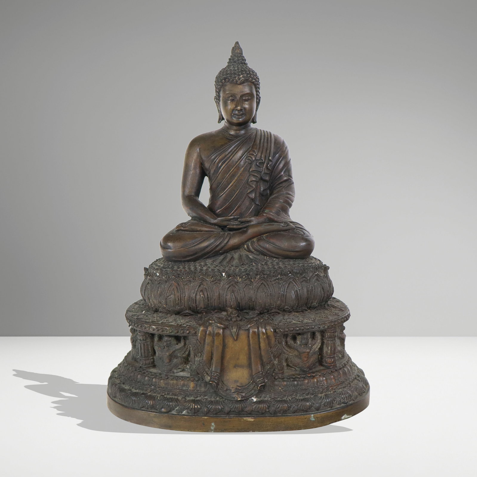 Chinese Bronze Seated Buddha: Chinese bronze seated buddha atop a lotus base, and second tier of small figures upholding platform with columns, buddha in a finely detailed robe. Weighted base. [12" H x 8" W x 6" D]. Good condition