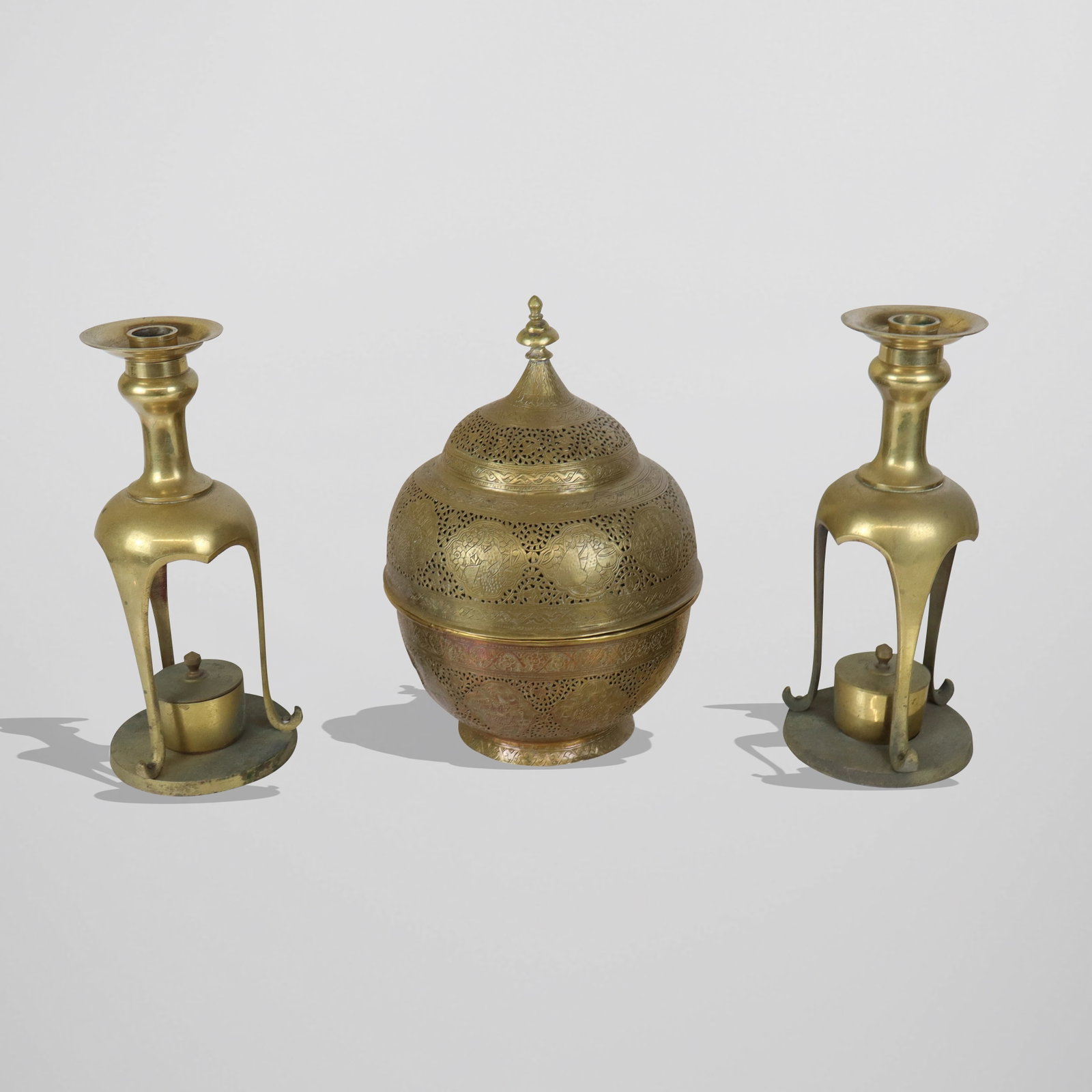 Three Indian Brass Table Decorations: Three Indian brass table decorations, pair candlesticks with lower covered burner pots [12" H x 5" diameter], and a pierced design covered incense burner jar with incised all around designs [12" H x 8