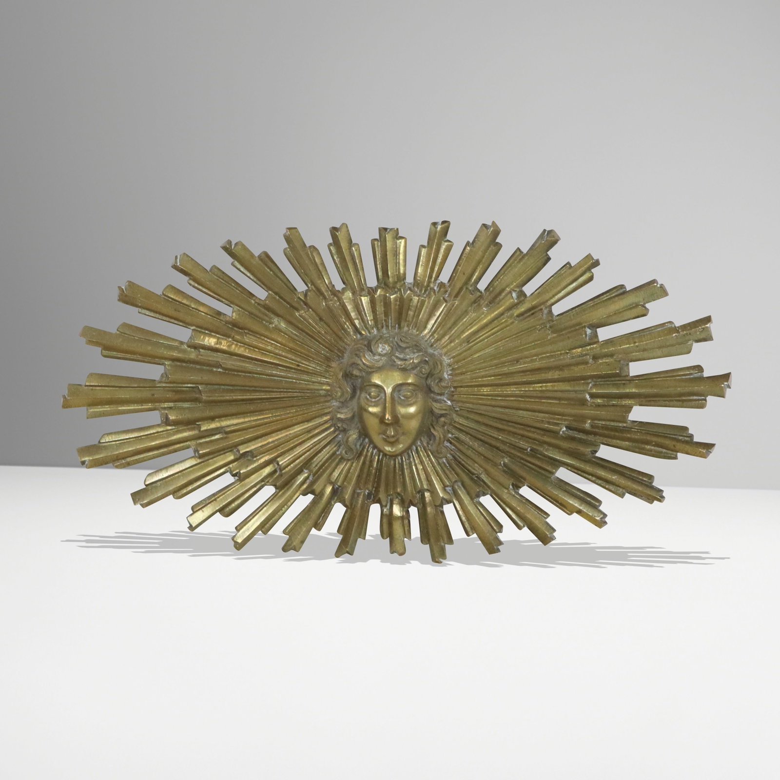Mid-Century Bronze Sunburst Plaque: Mid-Century bronze sunburst oval plaque, with facial center and bursts all around, holes on back for hanging. [9" H x 18" W]. Good condition, bottom burst slightly bent.
